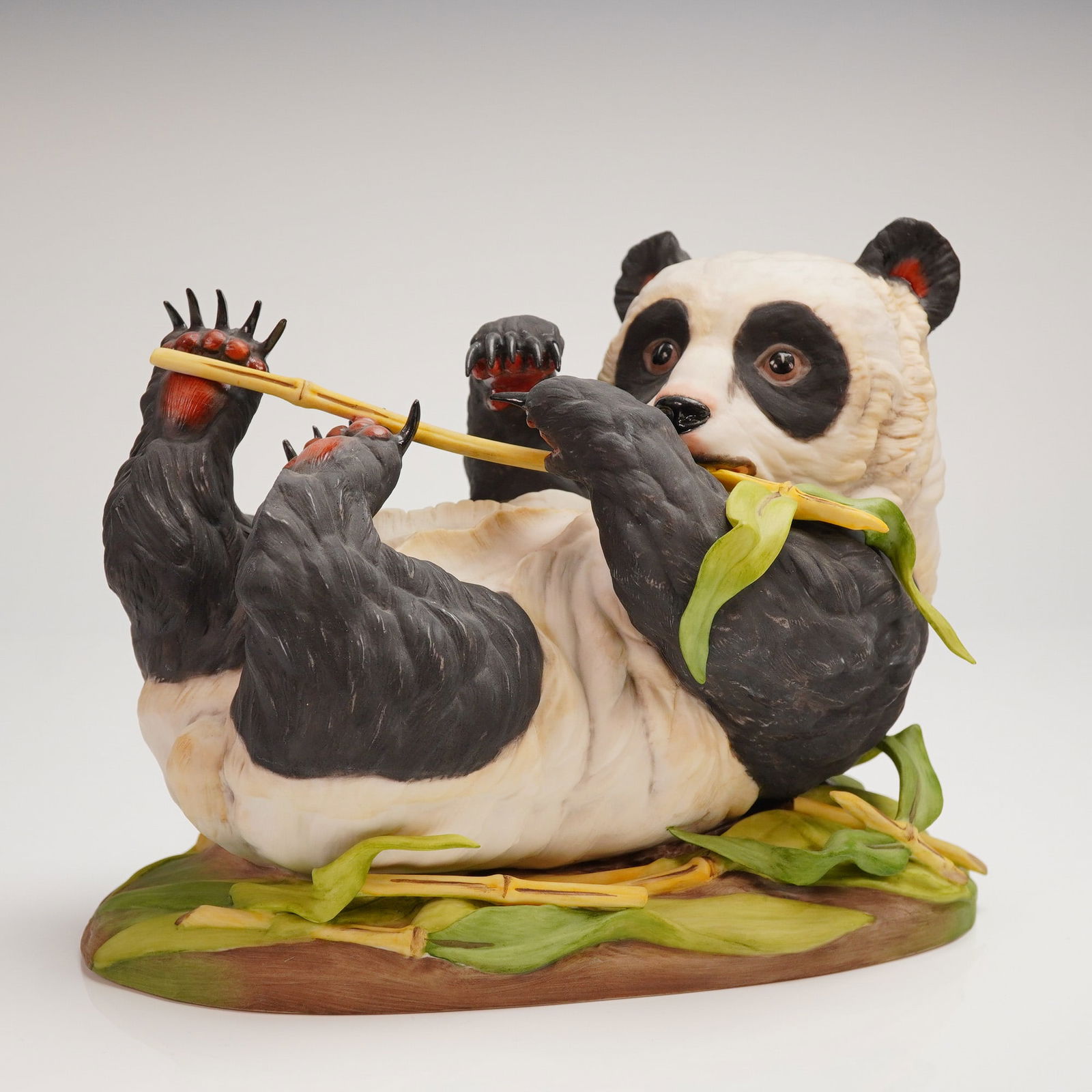 Edward Marshall Boehm Bone Porcelain Reclining Giant Panda Figurine: A single Edward Marshall Boehm Bone Porcelain figurine depicting a Giant Panda resting on its back and eating bamboo stalks. The sculpture features highly realistic modeling and a matte polychrome fin