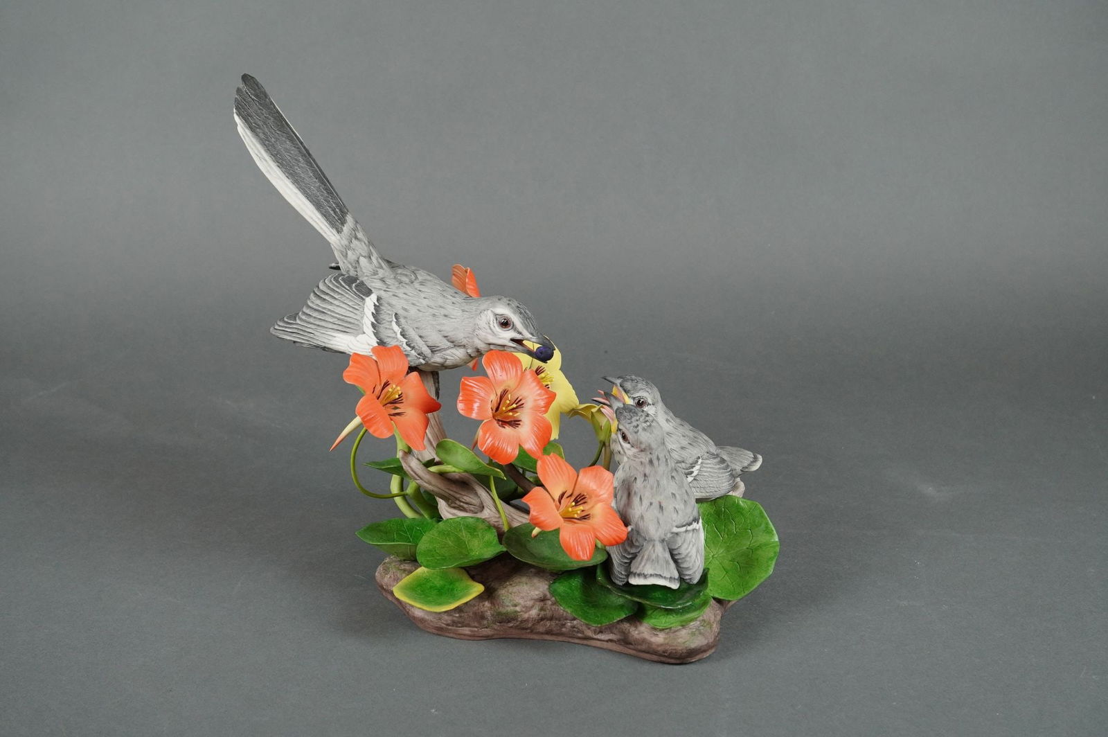 Edward Marshall Boehm Mockingbird Sculpture Ltd Ed. 1977: A single polychrome porcelain sculpture by Edward Marshall Boehm, depicting a naturalistic scene of Mockingbirds (mimus polyglottos). The composition features an adult Mockingbird feeding two nestling