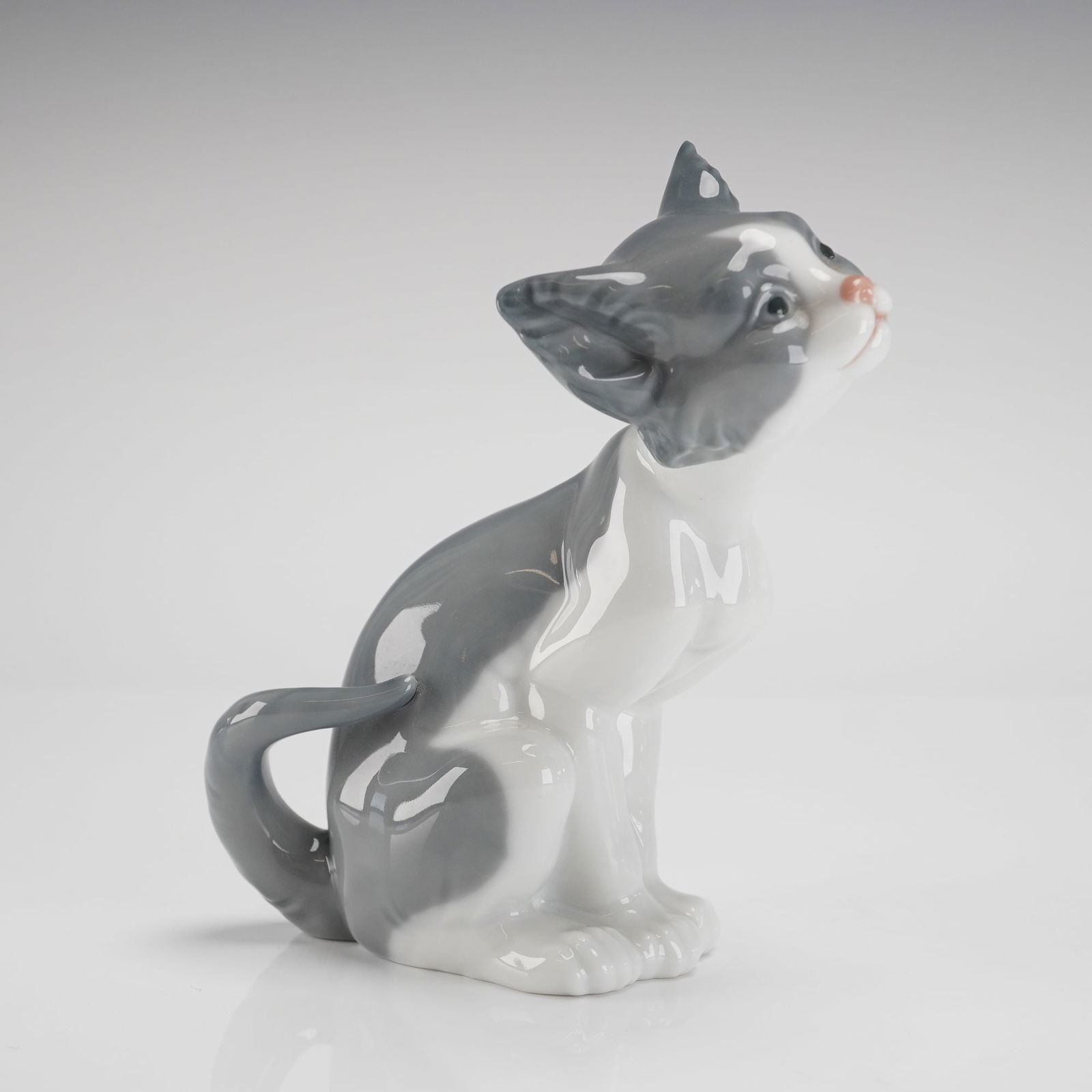 Lladro Porcelain Figurine Cat 1005113 Sculpted by Salvador Debon: A single glazed porcelain figurine depicting a sitting cat looking upwards with a curved tail, model 1005113. This Lladro Porcelain Figurine was sculpted by Salvador Debon and was issued between 1982