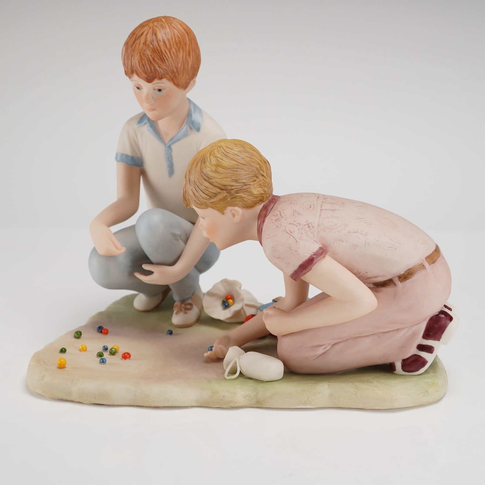 Cybis Porcelain Figurine Group Rusty and Jonny: A Cybis Porcelain Figurine depicting the figures known as Rusty and Jonny. This glazed porcelain figurine group features two young boys crouching on an integral base, engaged in playing marbles. The f