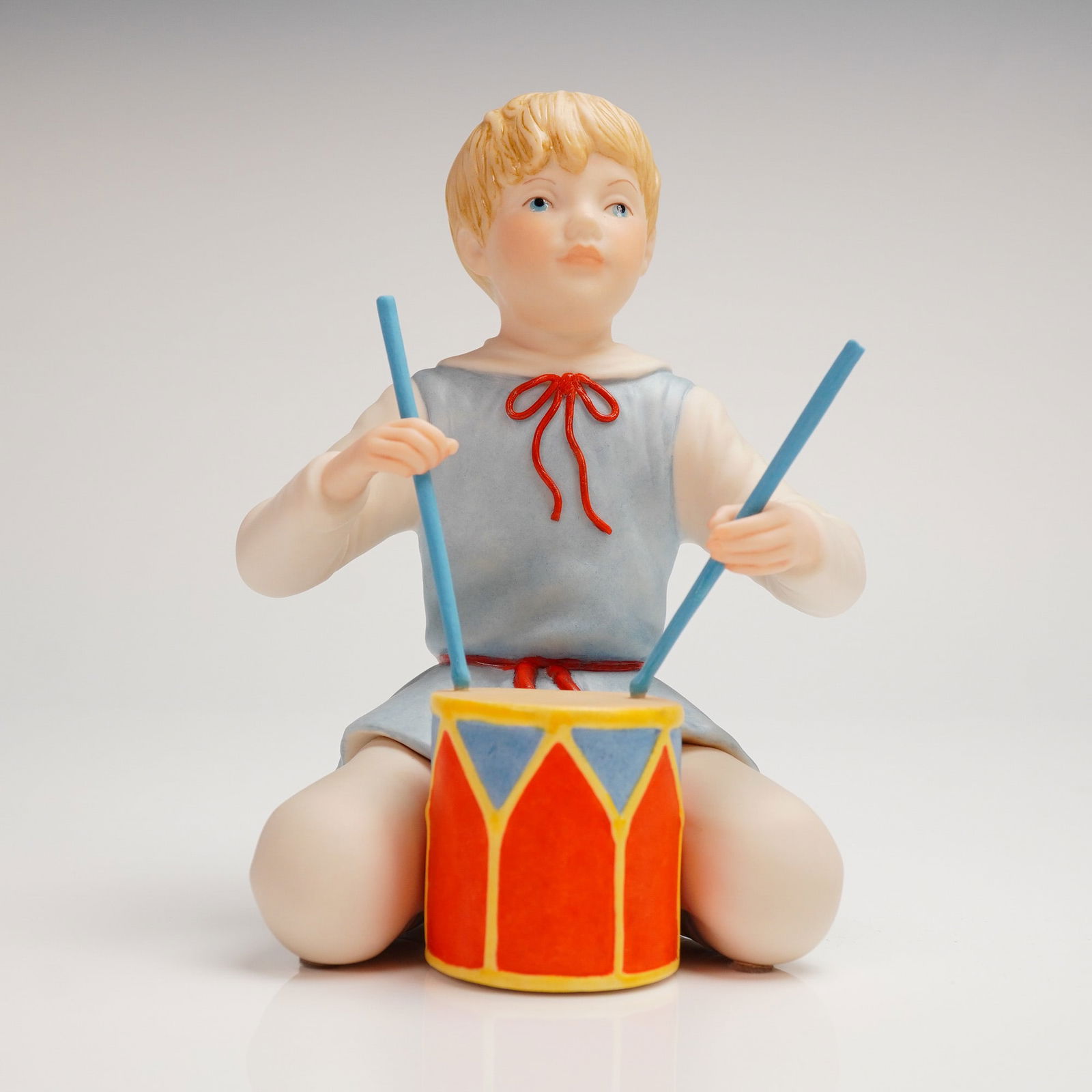 Vintage Cybis Matte Porcelain Drummer Boy Figurine: This is a single collectible bisque or matte porcelain figurine depicting a young, blond-haired child, identified thematically as a Drummer Boy. The figure is captured kneeling, poised to strike a bri