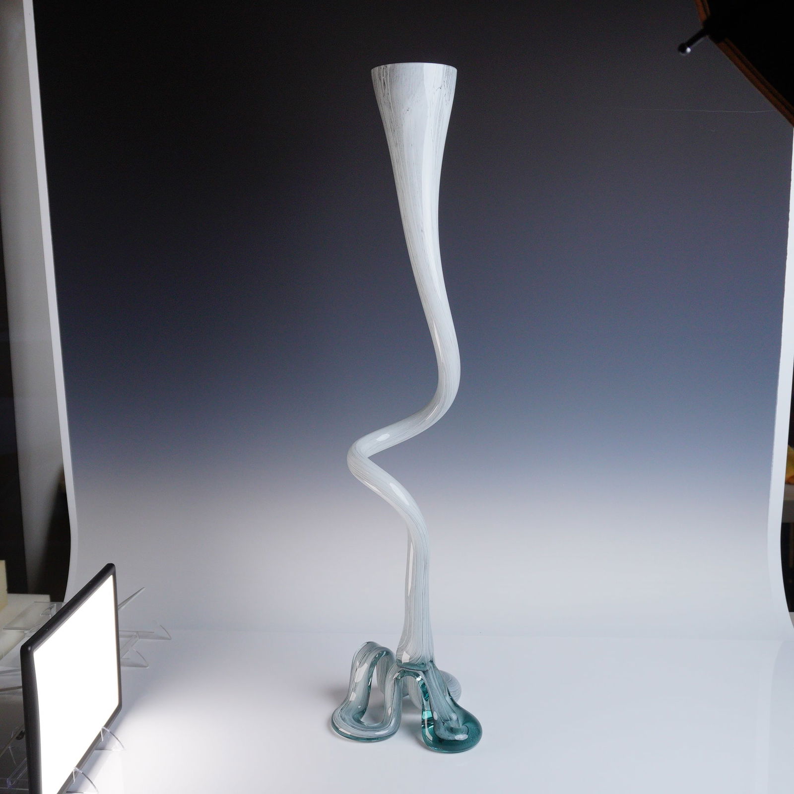 Murano Extra Tall Sculptural Art Glass Trumpet Vase: A contemporary art glass sculptural vessel executed in blown glass. The vase features a dramatically elongated neck rising from a complex, scrolling base. The body is predominantly white or opaline, d