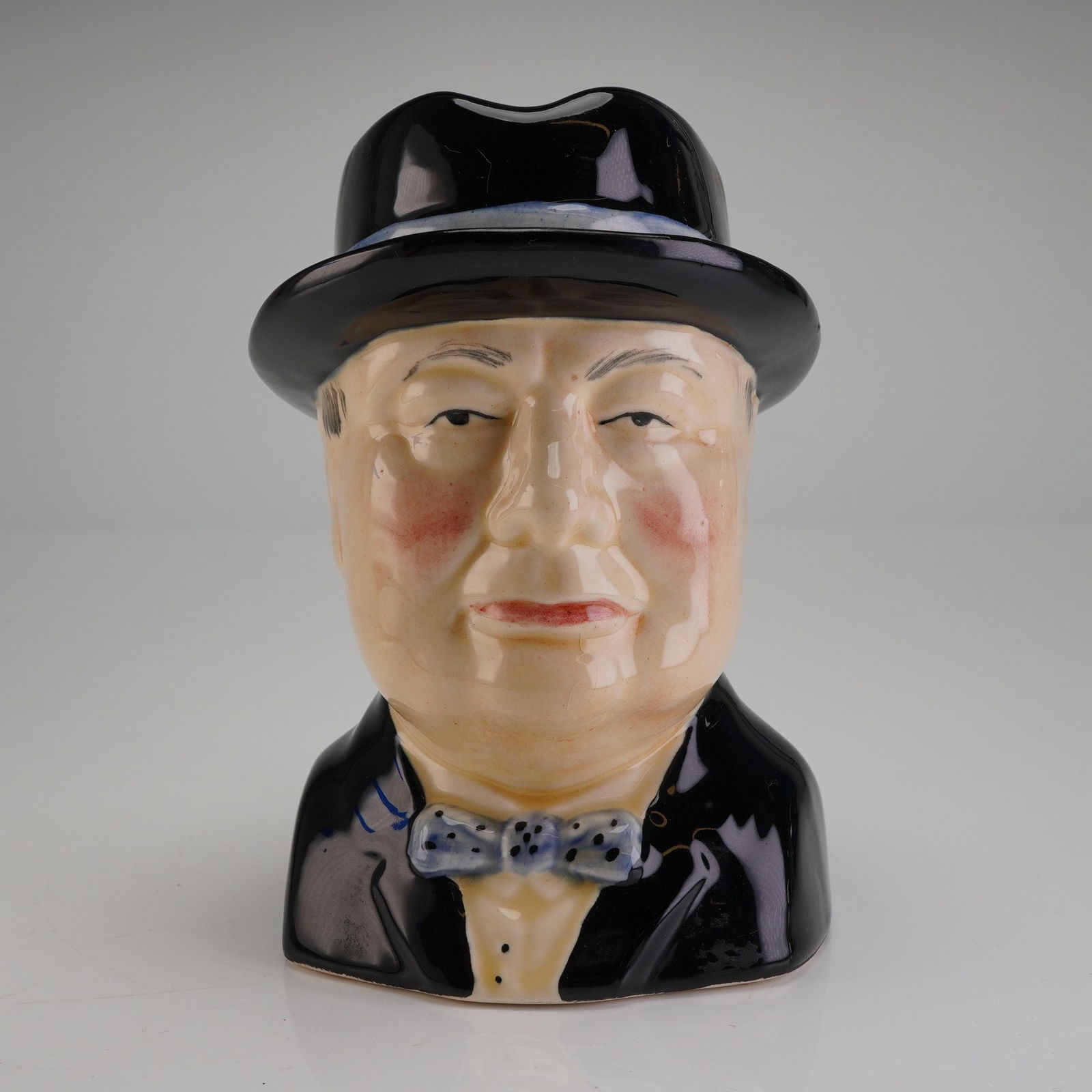 Wood Potters of Burslem Winston Churchill Character Jug: A hand-painted ceramic character jug produced by Wood Potters of Burslem in Staffordshire, England. The jug is modeled in the likeness of Winston Churchill, depicted wearing a black bowler hat, black