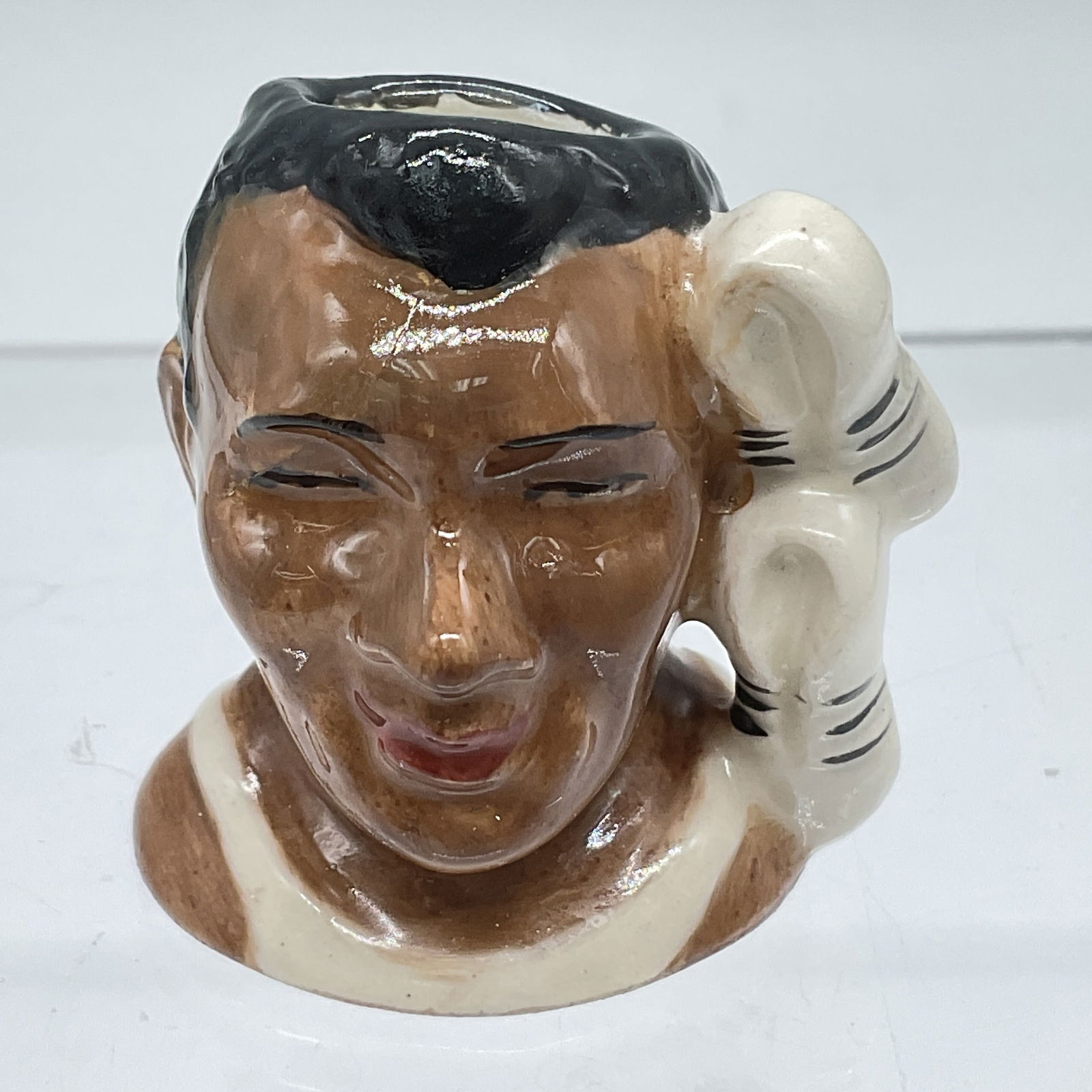 Royal Doulton Prototype Tiny Character Jug, Jesse Owens: A hand painted figural jug of the American track and field athlete. He won four gold medals at the 1936 Olympic Games. The tiny jug shows the athlete in a white track top, and his white and black snea