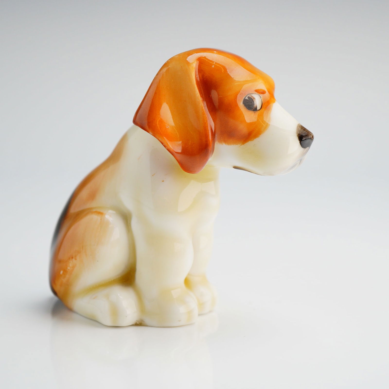 Doulton Porcelain Figurine, Rare Beagle Puppy: The figurine features tri-color dog, painted in white, bright orange-tan, and dark brown/black patches. The dog is modeled in a seated position with its head slightly lowered. The base is marked 'Doul