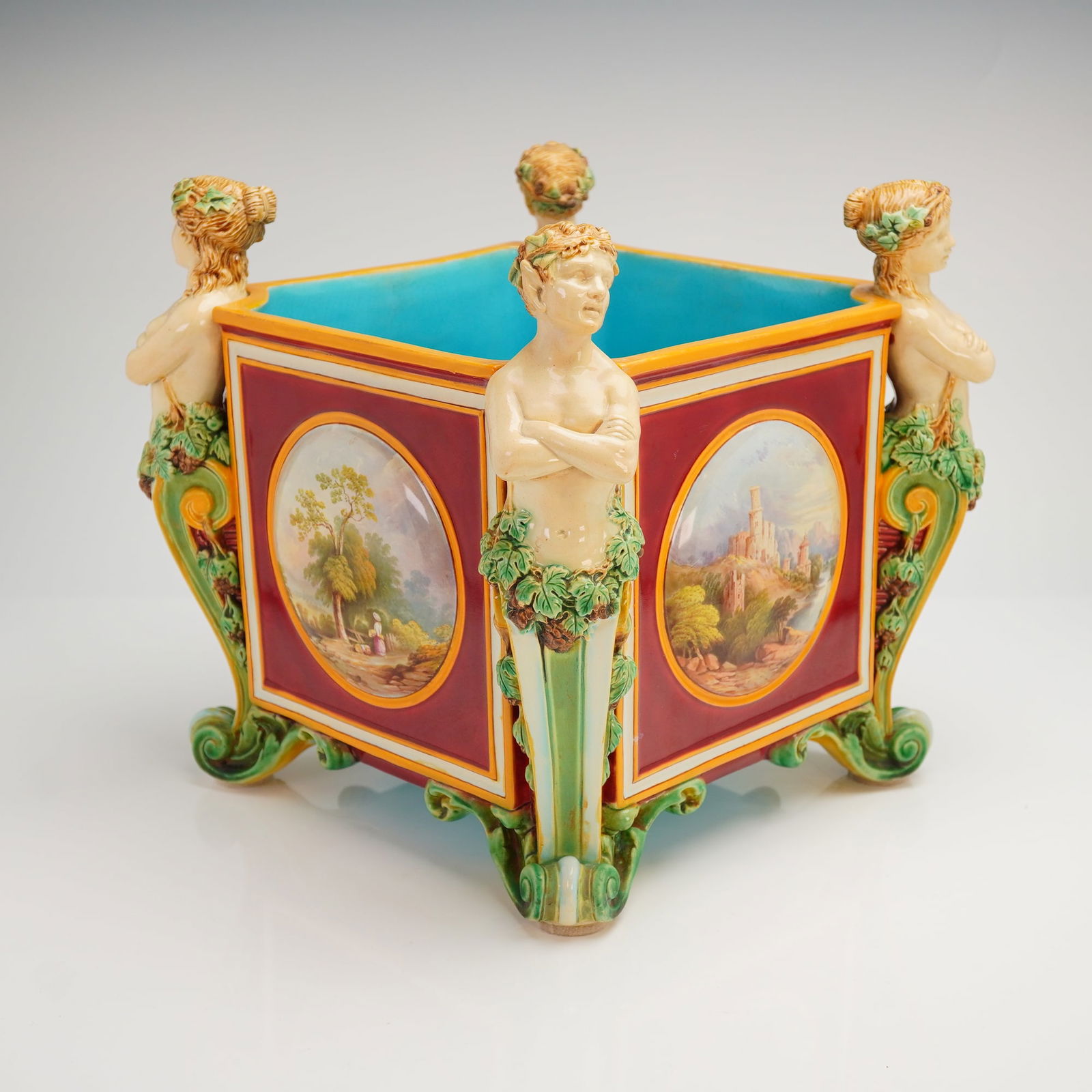 Minton Majolica Thorwaldsen Jardiniere: A square-form jardiniere, set on four intricately modeled legs representing half-length figures of two male satyrs and two female nymphs, their arms crossed and lower bodies entwined with vine and gra