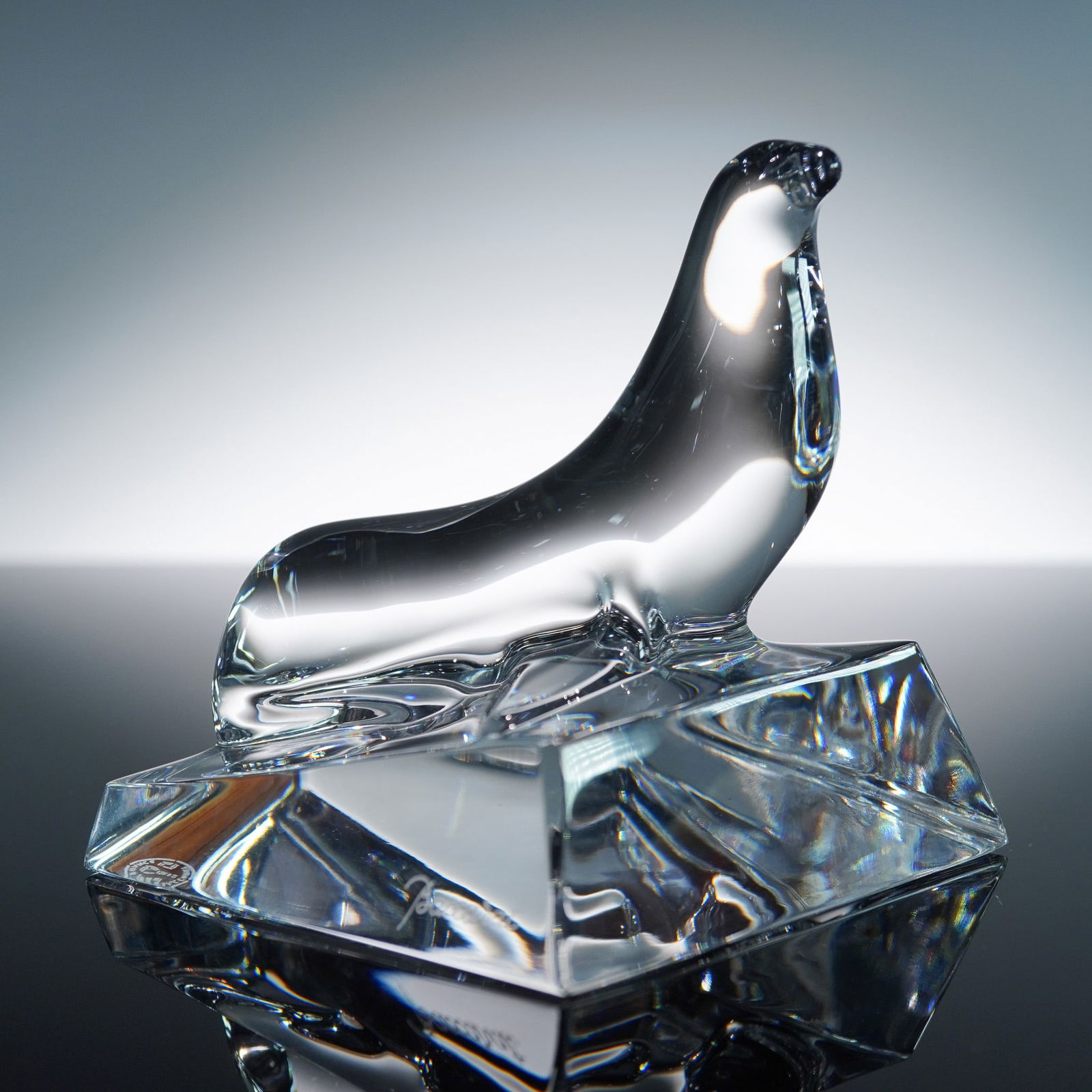Baccarat Crystal Figurine, Seal: A sculptural crystal seal poised atop a sharply faceted base, showcasing the unparalleled mastery of form and clarity. The seal's fluid silhouette is rendered in gleaming clear crystal, its contours c