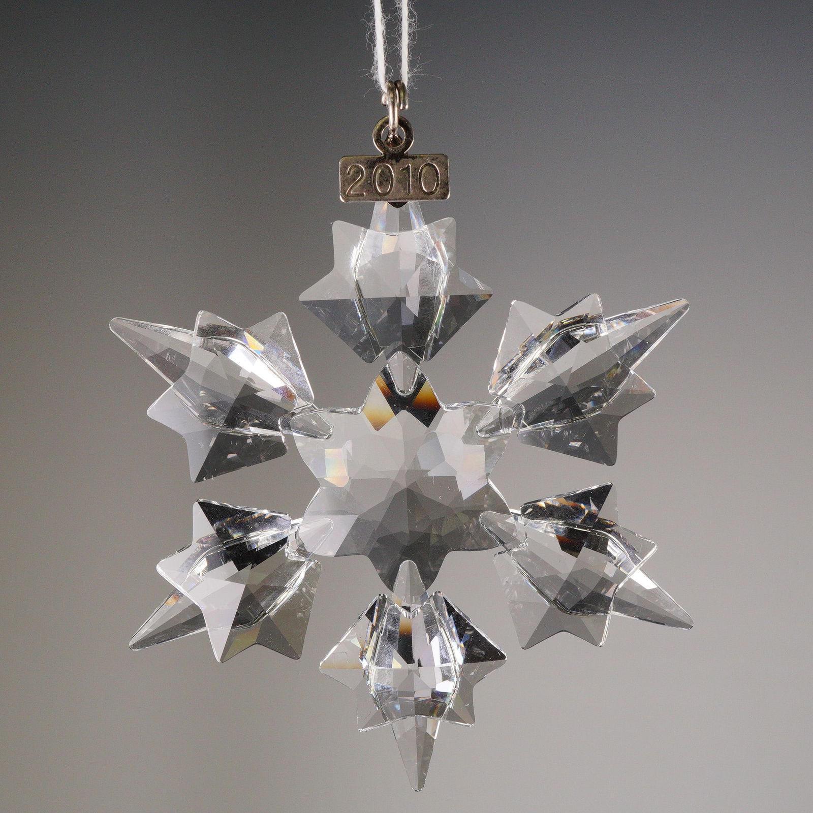 Swarovski Annual Edition 2010 Crystal Snowflake Ornament: A crystal ornament produced by Swarovski for their Annual Edition Christmas series, dated 2010. The ornament is crafted in the form of a six-pointed snowflake with complex, sharp faceting designed to