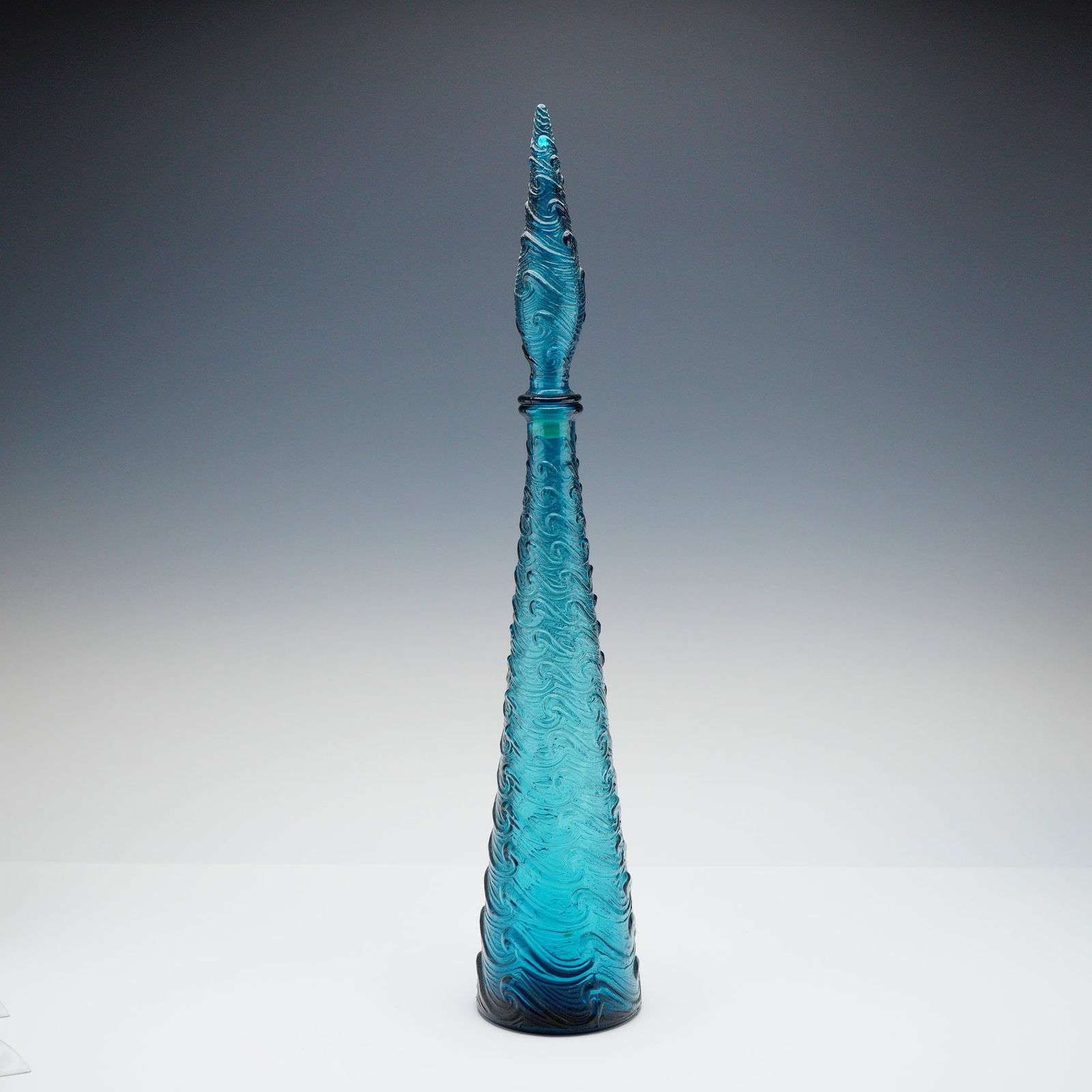 Italian Mid-Century Modern Glass Decanter and Stopper: This lot comprises a decanter and its matching stopper. The set is executed in vibrant translucent teal blue molded glass. The decanter features a tall, slender conical body rising to a narrow neck. B