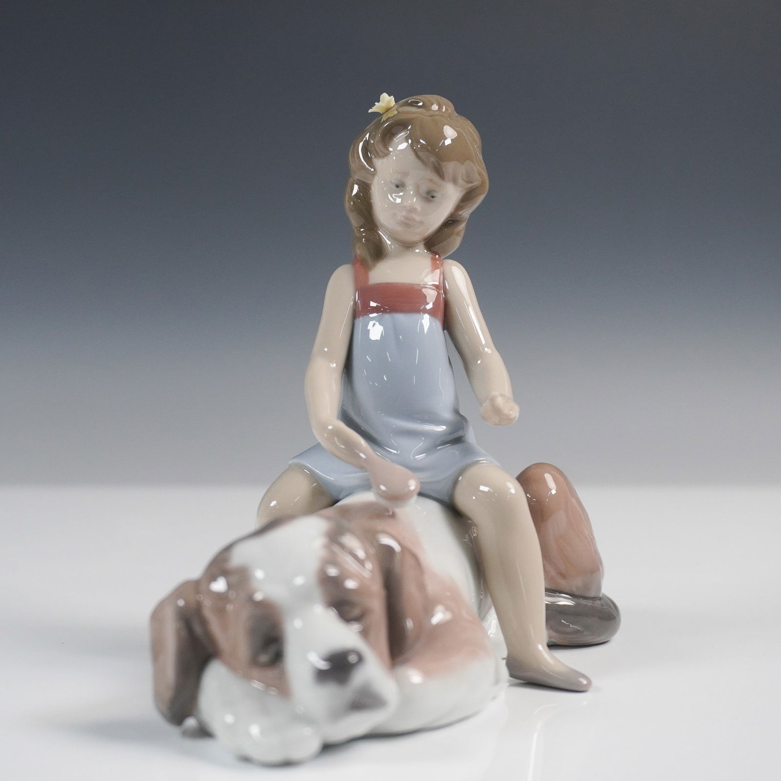 Lladro Porcelain Figurine Contented Companion 01006229: Lladro porcelain figurine titled Contented Companion, model 01006229, sculpted by Juan Huerta. Issued in 1995 and retired in 2001, it features a young girl gently brushing a large, resting Saint Berna