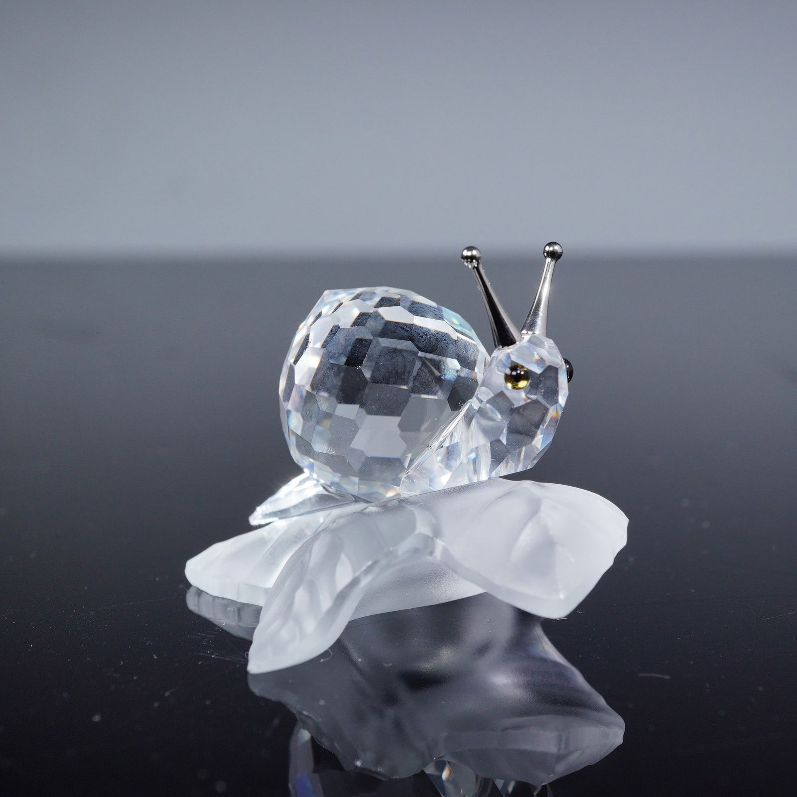Swarovski Crystal Figurine, Snail on Leaf, Model 196501: A Swarovski crystal figurine depicting a snail on a leaf, model 196501. The snail's shell is crafted from multi-faceted clear crystal, while its stylized body and leaf-shaped base are made of frosted