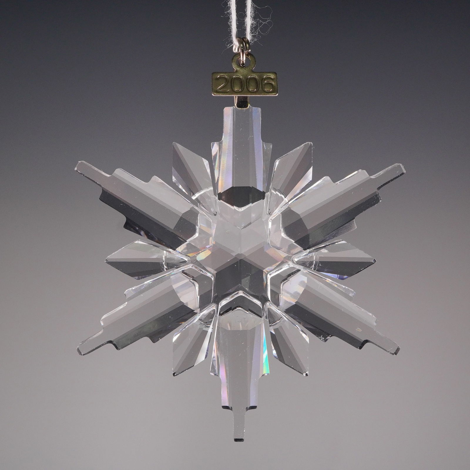 Swarovski Annual Edition 2006 Crystal Snowflake Ornament: This clear, highly faceted crystal is cut in a complex twelve-point snowflake. Hanging from the fitting is tag engraved with "2006" confirming its year of issue. The reverse side of the fitting is mar