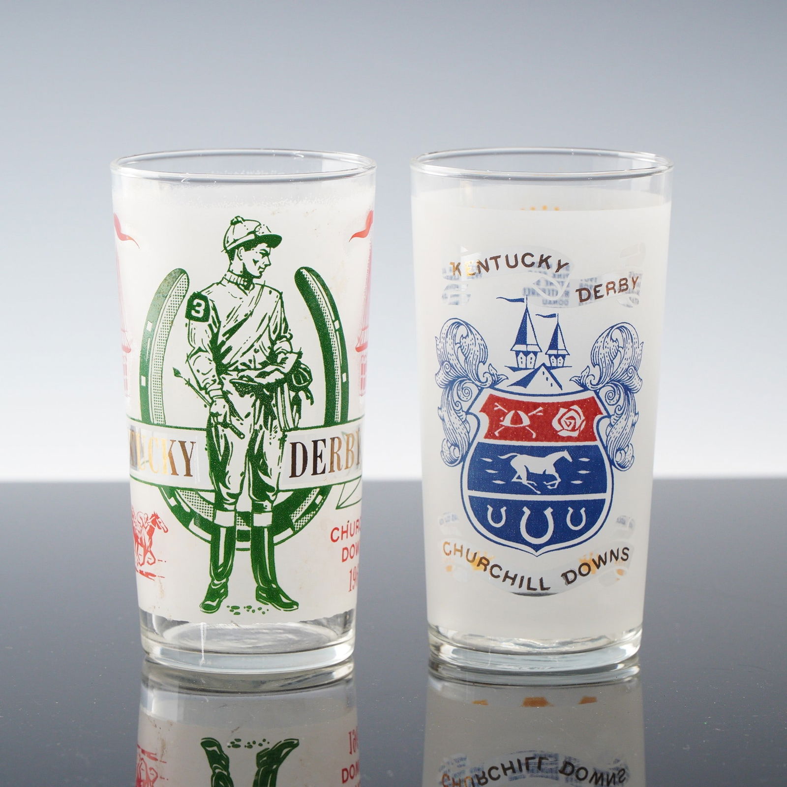 2pc Kentucky Derby Commemorative Glasses, Churchill Downs: Two Kentucky Derby commemorative glasses from Churchill Downs, celebrating the history and tradition of one of America's most iconic sporting events. One glass features a bold green and red design wit