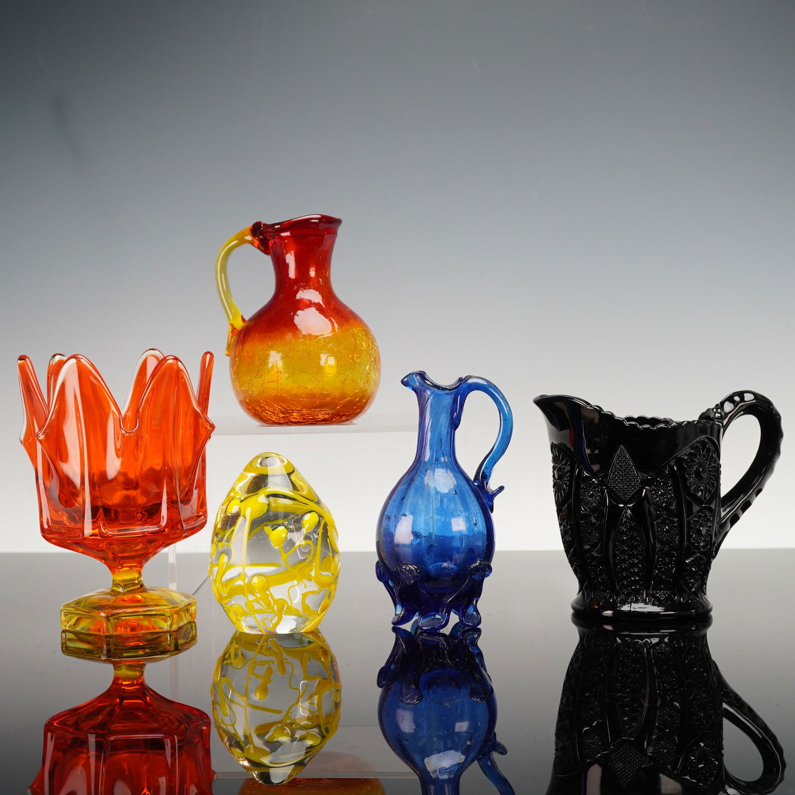 5pc Glass Colored Vases, Jugs, and Paperweight: This 5 piece grouping combines both decorative and functional colored glass forms, including a vivid orange pedestal vase with a flared sculptural rim, a warm amber crackle glass jug, a hand blown blu