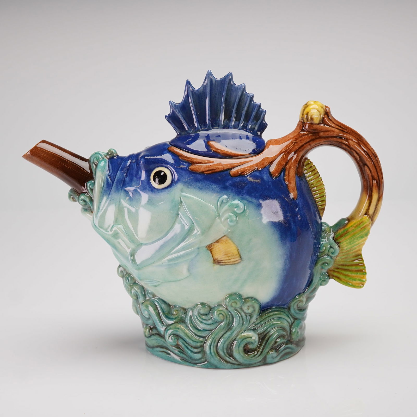 Minton Archive Fish Teapot with Lid: A Minton Archive Collection Fish Teapot, executed in glazed Fine China. The novelty teapot is modeled in the form of a large marine fish rising from sculpted green waves that form the base. The body i