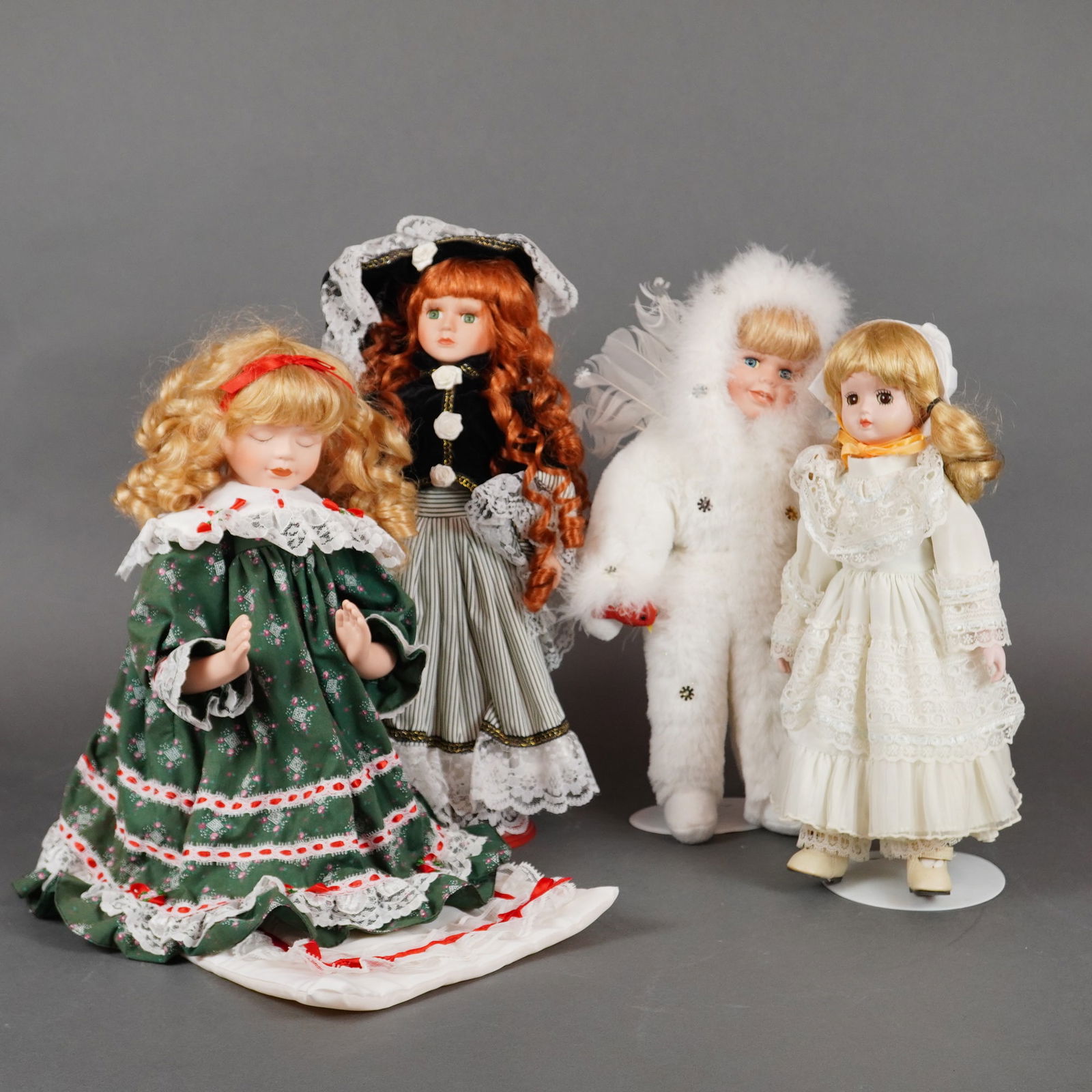 A Collection of Four Collector Porcelain Dolls: A collection of four collector display dolls, featuring porcelain heads and possibly limbs, with soft textile bodies. The dolls are dressed in elaborate textile costumes incorporating lace, ribbons, a