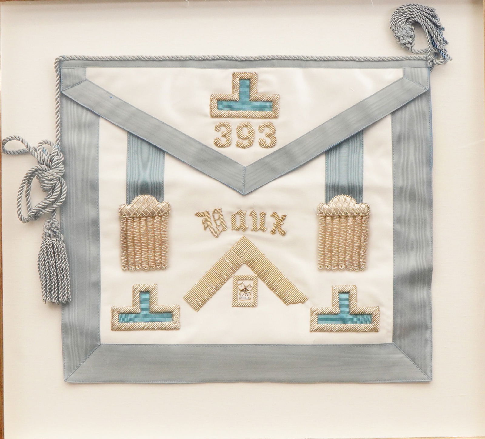 Ornate Framed Masonic Ceremonial Apron for Lodge 393 VAUX: A single ceremonial item, a Freemason masonic apron, framed under glass. The apron is constructed on a cream-colored silk or satin ground fabric, featuring light blue/silver moire silk ribbons used fo