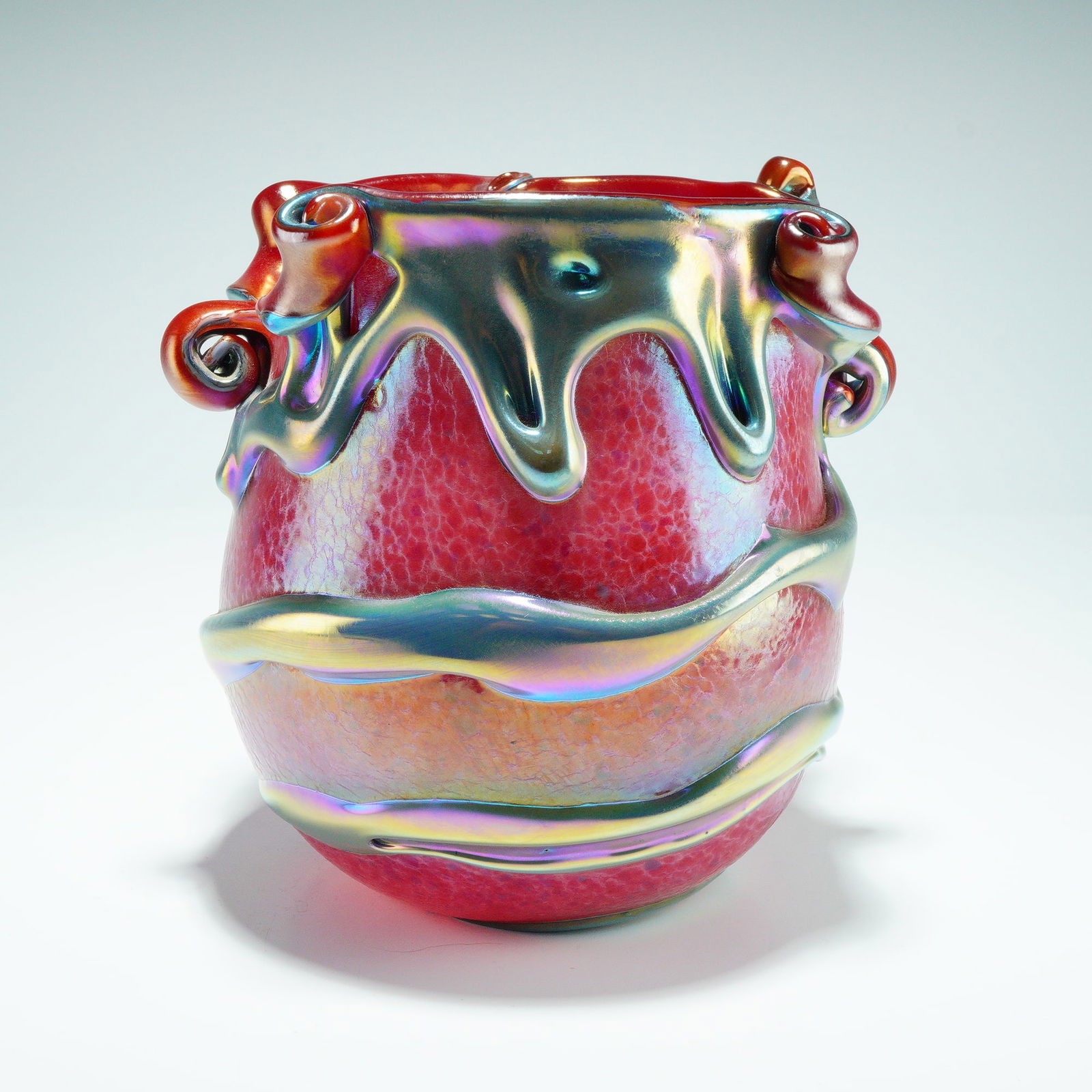 Charles Lotton Studios Lava Cypriot Glass Vase: A red glass vase featuring a mottled, crackled surface texture and applied iridescent Lava-style trails layered around the body. The rim is formed with an undulating, uneven edge accented by applied s