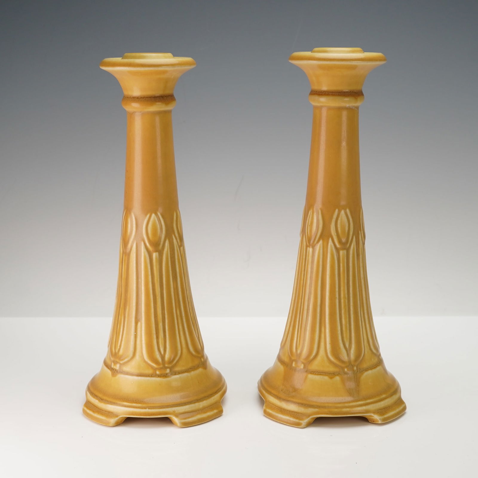 A Pair of Rookwood Pottery Candlesticks, Shape 1630: A pair of Rookwood Pottery candlesticks, Shape 1630, dated 1920. Each candlestick features a tapered, columnar form finished in a warm mustard yellow or ochre hue, exhibiting a subtle crackle glaze. T