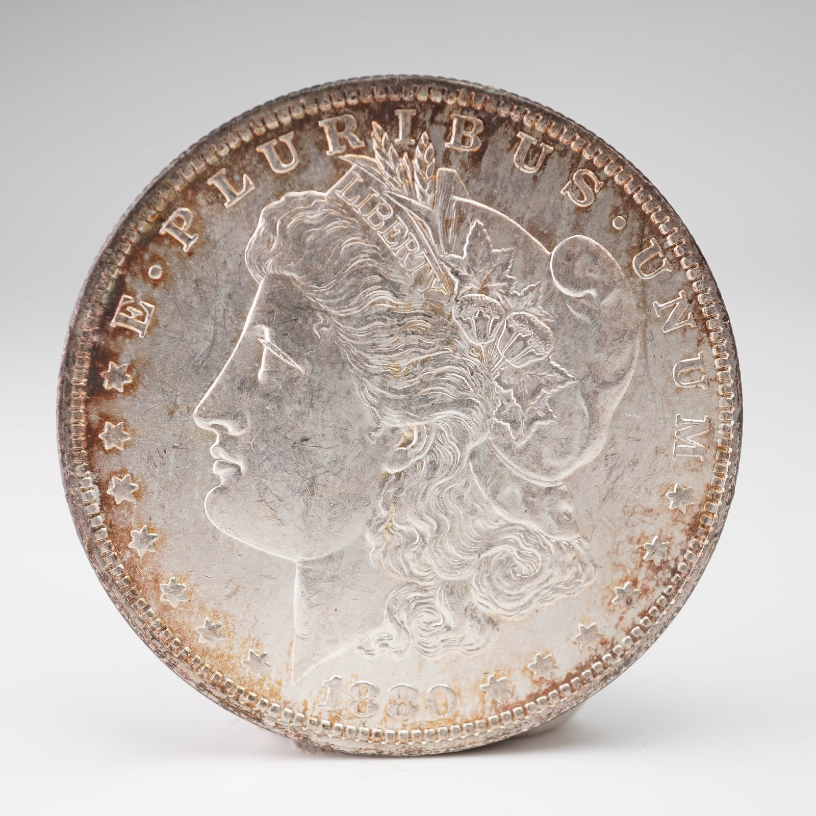 1880-O Morgan Silver Dollar: An 1880-O Morgan Silver Dollar, minted at the New Orleans facility and composed of ninety percent silver. The obverse displays Liberty wearing a Phrygian cap adorned with wheat and cotton, emblematic 
