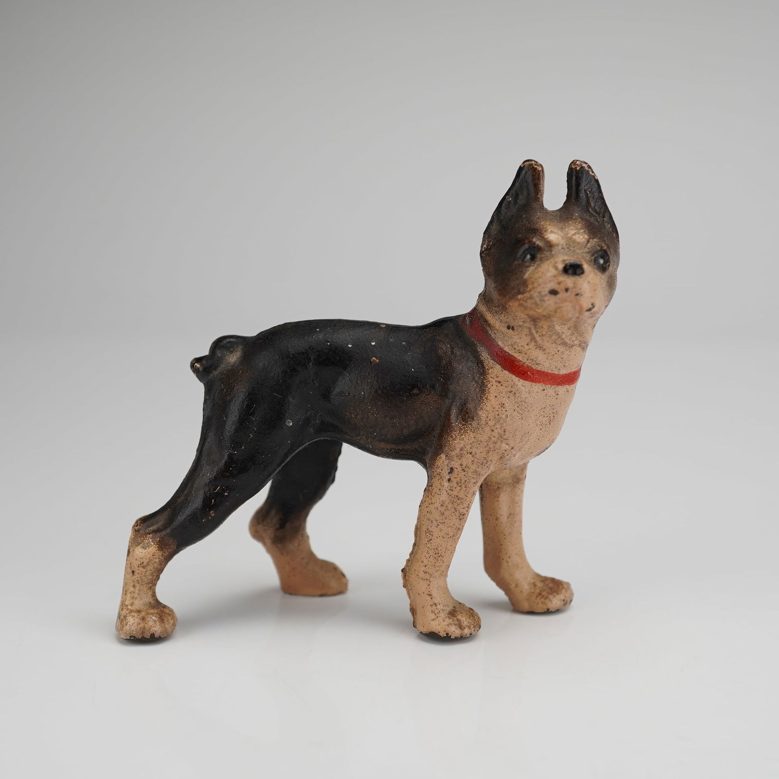 Hubley Cast Iron Boston Terrier Figurine Paperweight: A cast iron figurine modeled as a Boston Terrier. The object is constructed of heavy cast iron and features a hand-painted finish in black and tan, accented by a painted red collar. The dog is depicte