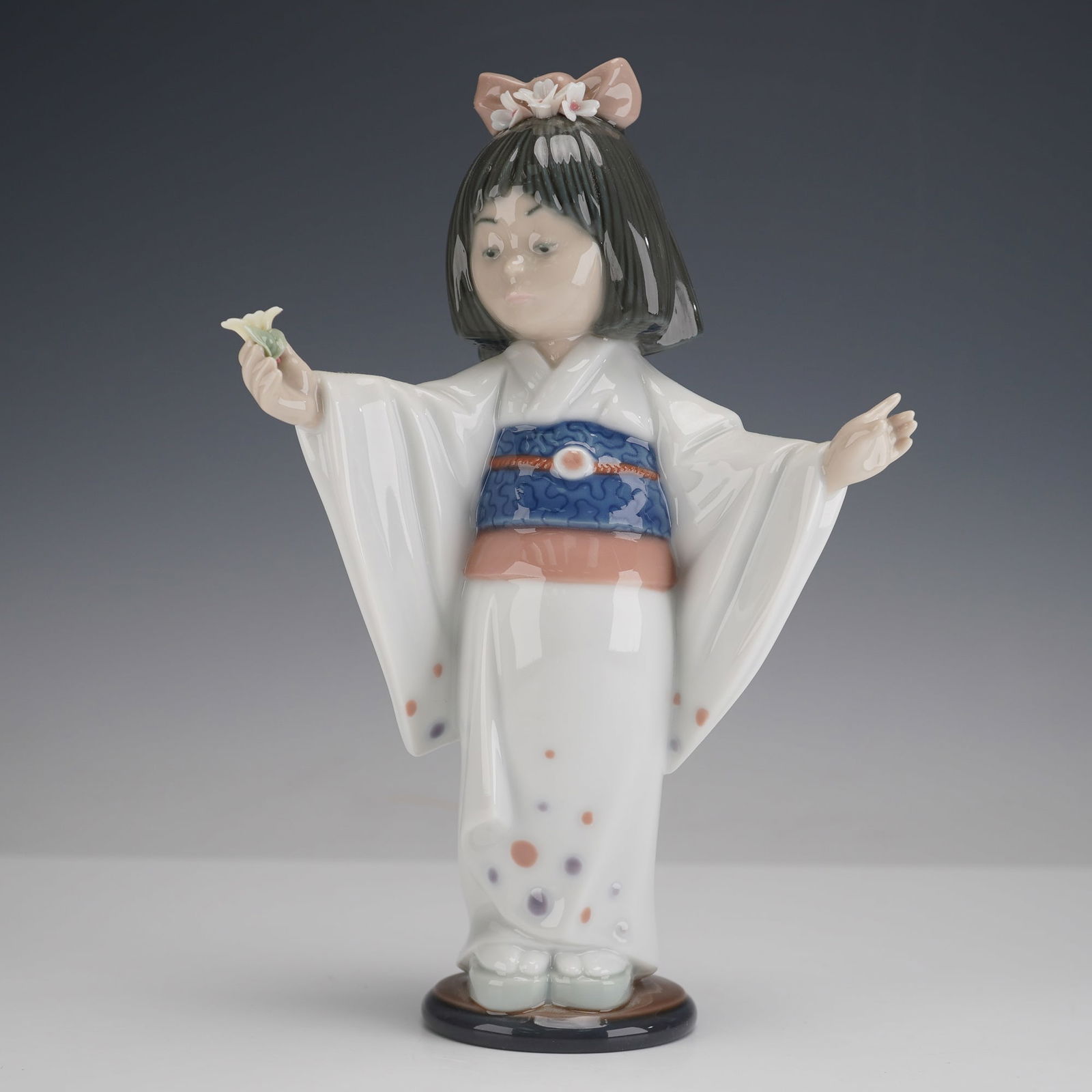 Lladro Porcelain Figurine, Flower Gazer 1006152: Glazed porcelain Lladro figure model 6152 depicting a young girl in a patterned kimono holding a small flower, on circular dark blue base, the underside with printed Lladro hand made in Spain backstam