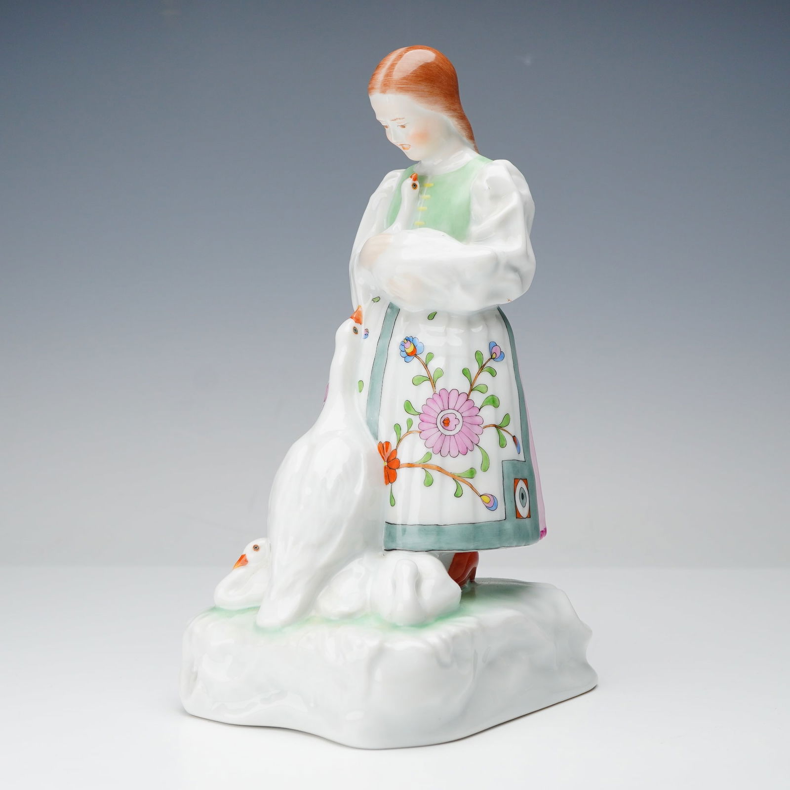 Herend Porcelain Figurine, Girl With Geese: Figurine of a woman in a traditional dress offering food to a goose, hand painted in bright folk-style colors. Herend Hungary backstamp on the underside. Dimensions: 3.5"L x 4.5"W x 7.75"H Country of