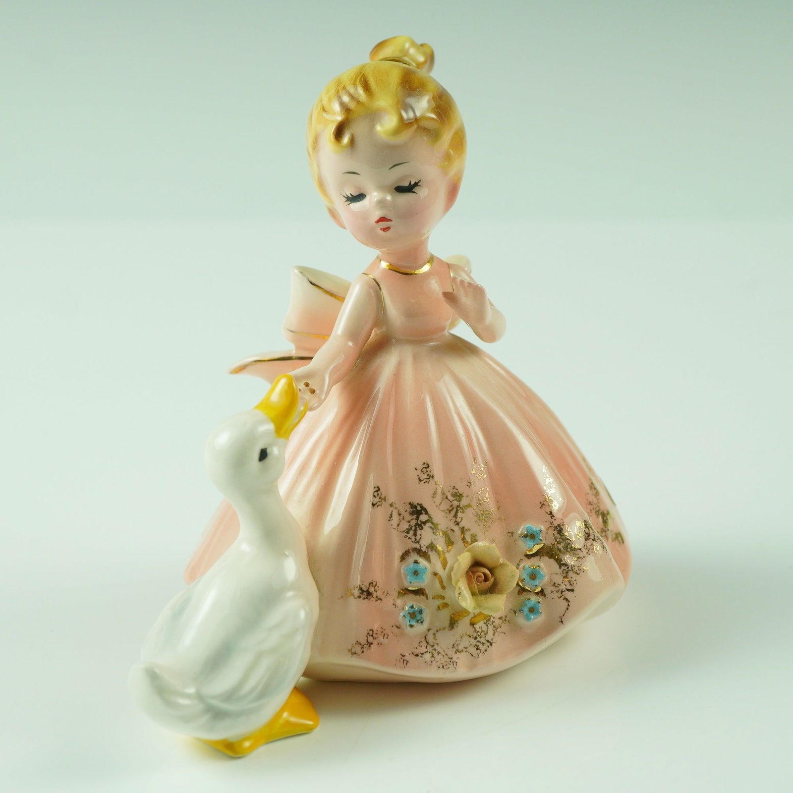 Vintage Josef Originals Porcelain Figurine, Girl with Duck: This charming Josef Originals figurine features a young blonde girl in a flowing pink dress adorned with delicate floral detailing and gold accents. She is depicted with a sweet expression as she gent