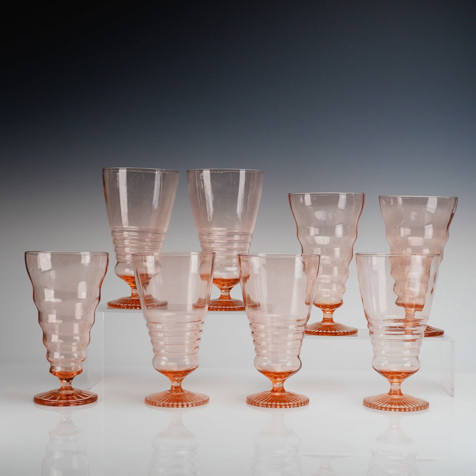 8pc Pink Depression Glass Soda Fountain Goblets, Diamond Leaf Rays Pattern: Soda fountain goblets, executed in molded Pink Depression Glass. Four glasses exhibit pronounced horizontal ribbing around the lower bowl, while the other four show a slightly wavy, tapered profile. A