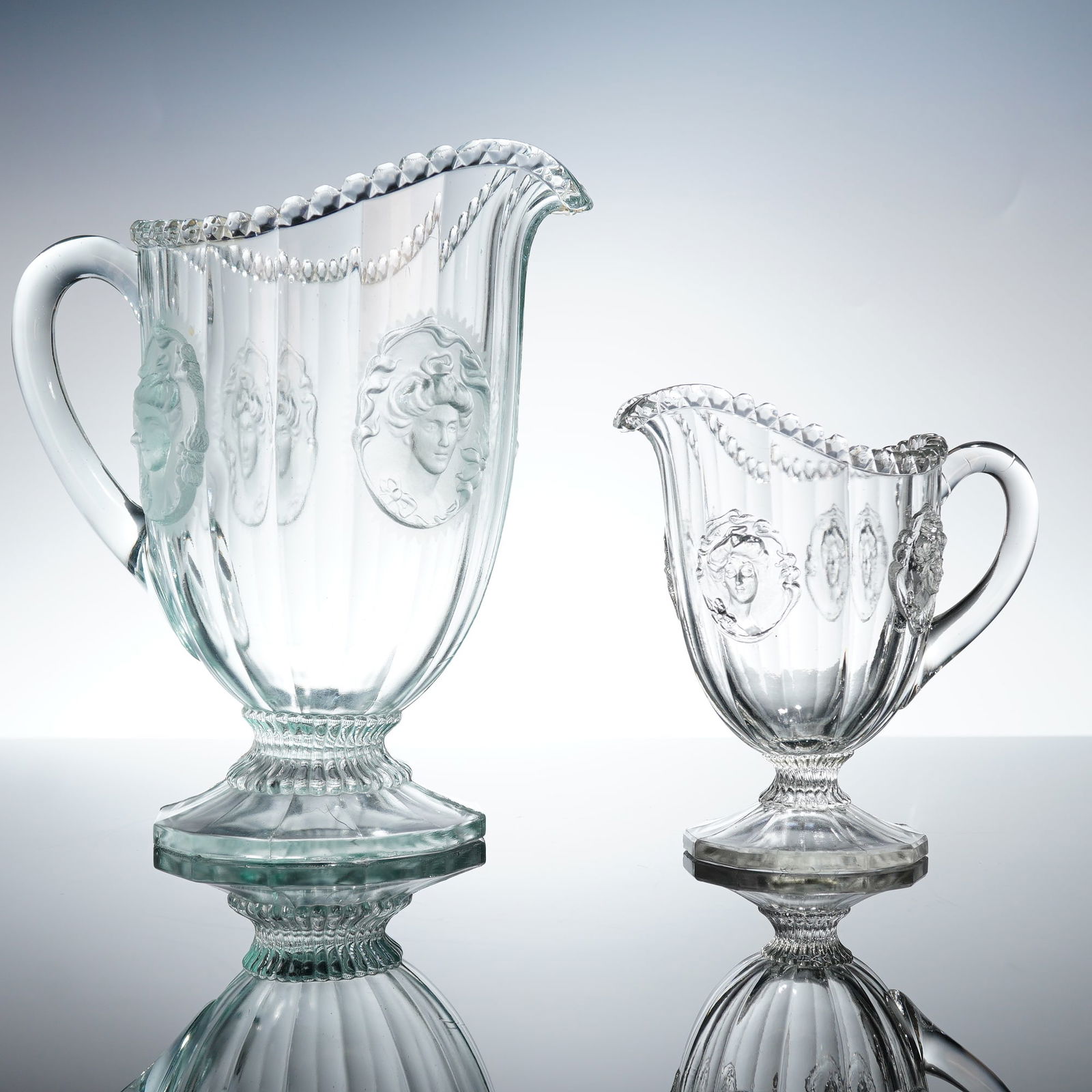 Pair of National Glass Co Pressed Glass Gibson Girl Pitcher and Creamer: The lot includes two distinct etched patterns. The first pitcher is attributed to the Greentown Glass Company, featuring the Squirrel pattern, depicting a bird or squirrel nestled within leafy branche