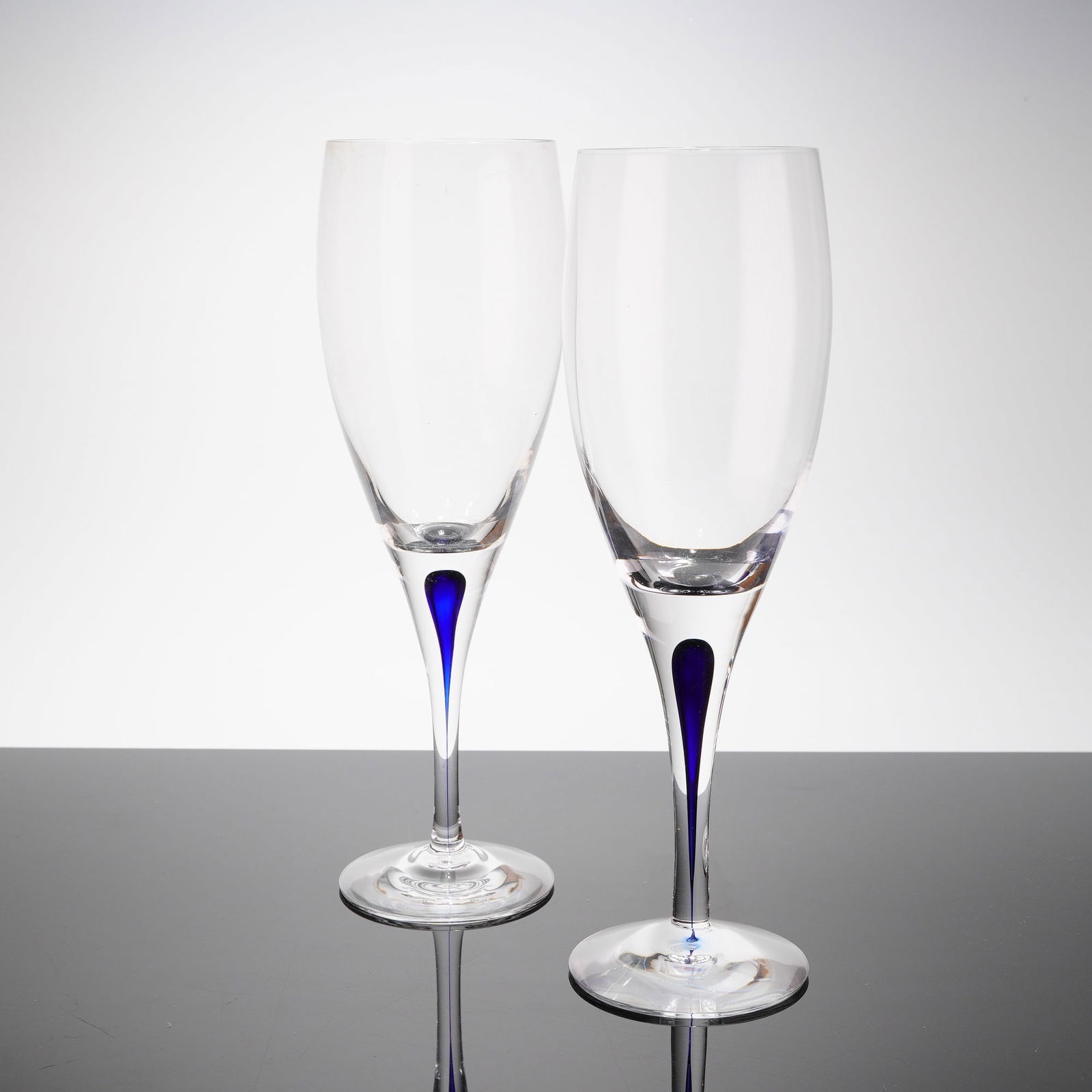 A Pair of Orrefors Intermezzo Blue Claret Wine Glasses: A pair of Orrefors Intermezzo Blue crystal champagne fi‚utes. These contemporary drinkware pieces, often referred to as 2pc Orrefor Crystal Intermezzo wine glasses, feature a tall, slender bowl atop