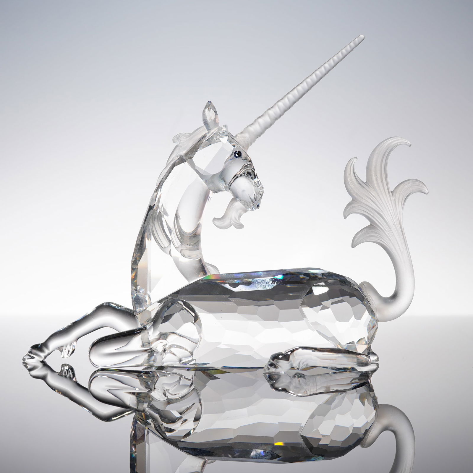 Swarovski 1996 Fabulous Creatures Crystal Figurine, Unicorn: A Swarovski SCS 1996 Annual Edition 'Fabulous Creatures' Unicorn, model 191727. Clear faceted crystal depicting a recumbent unicorn with a single horn and stylized tail. Blue crystal eyes. Underside e