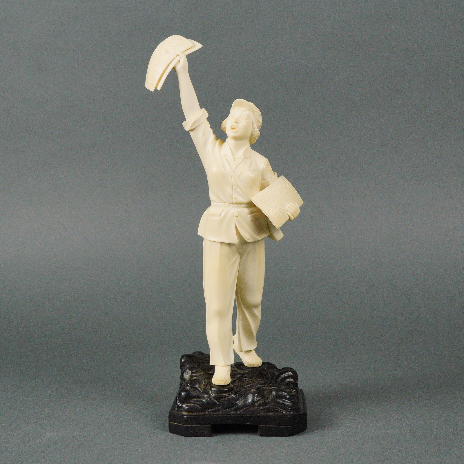 Carved Bone Chinese Revolutionary Figure with Newspapers on Wooden Base: Finely carved figural sculpture depicting a Chinese revolutionary figure, shown standing atop a stylized base and dramatically raising a folded newspaper overhead while holding additional papers under
