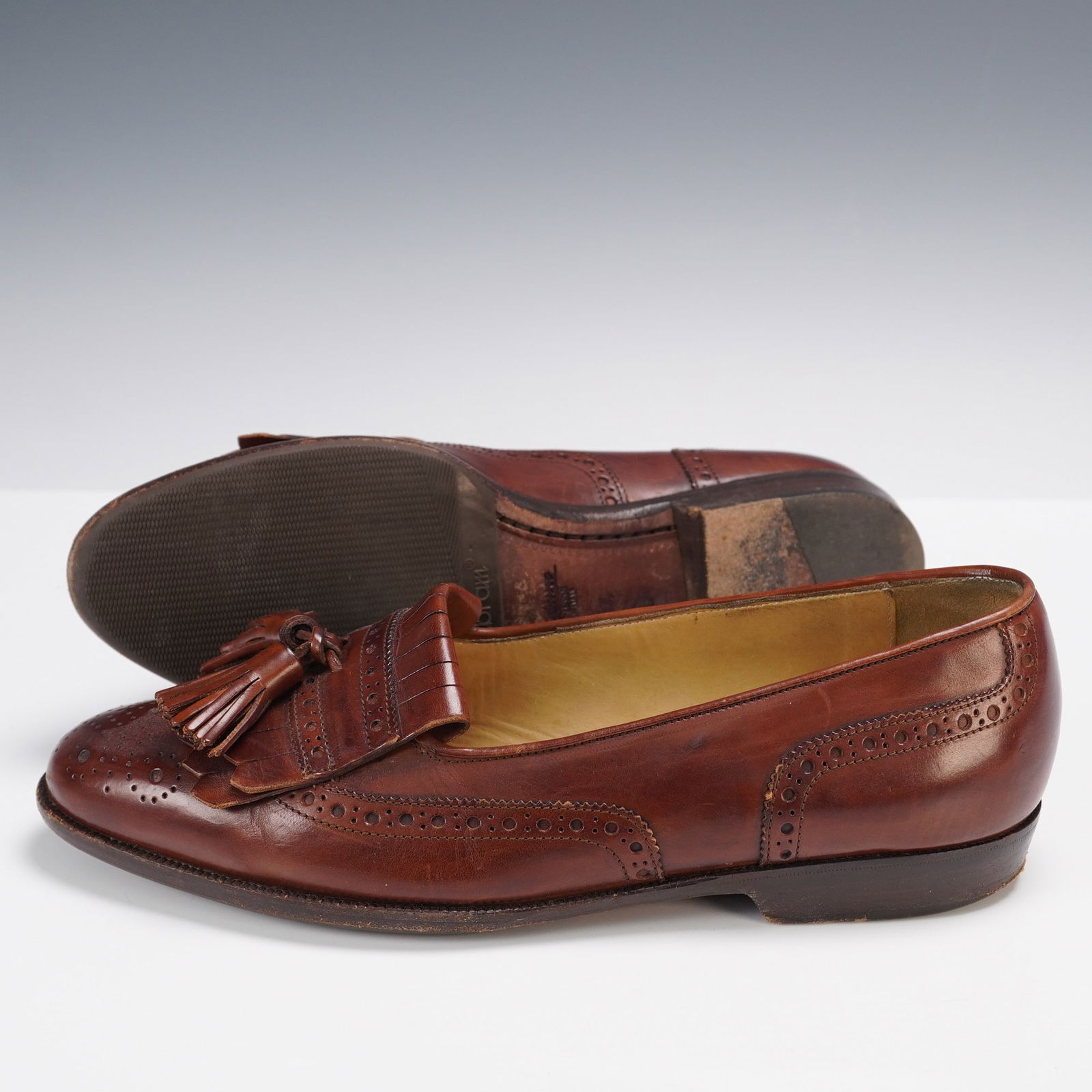 Bragano by Cole Haan Brown Leather Tassel Loafers: A classic and refined pair of men's tassel loafers by Bragano for Cole Haan, crafted in Italy from rich brown leather. These shoes feature traditional broguing along the toe and sides, a hand-stitched