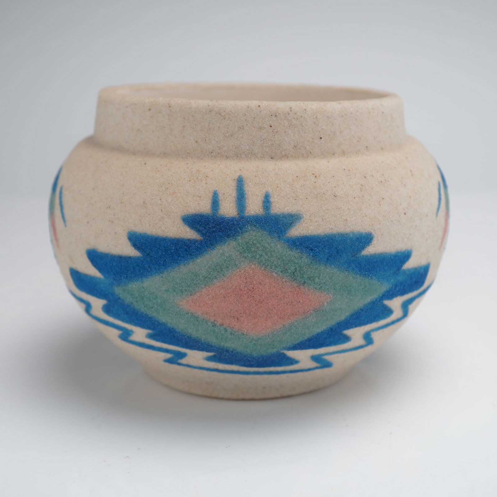 Sunwest Arts Ltd. Navajo Sand Art Pottery Vase and Tag: A piece of Navajo Sand Art Pottery produced by Sunwest Arts, Ltd. The squat vessel is constructed of ceramic material finished with a highly textured, coarse sand application in a natural beige tone.