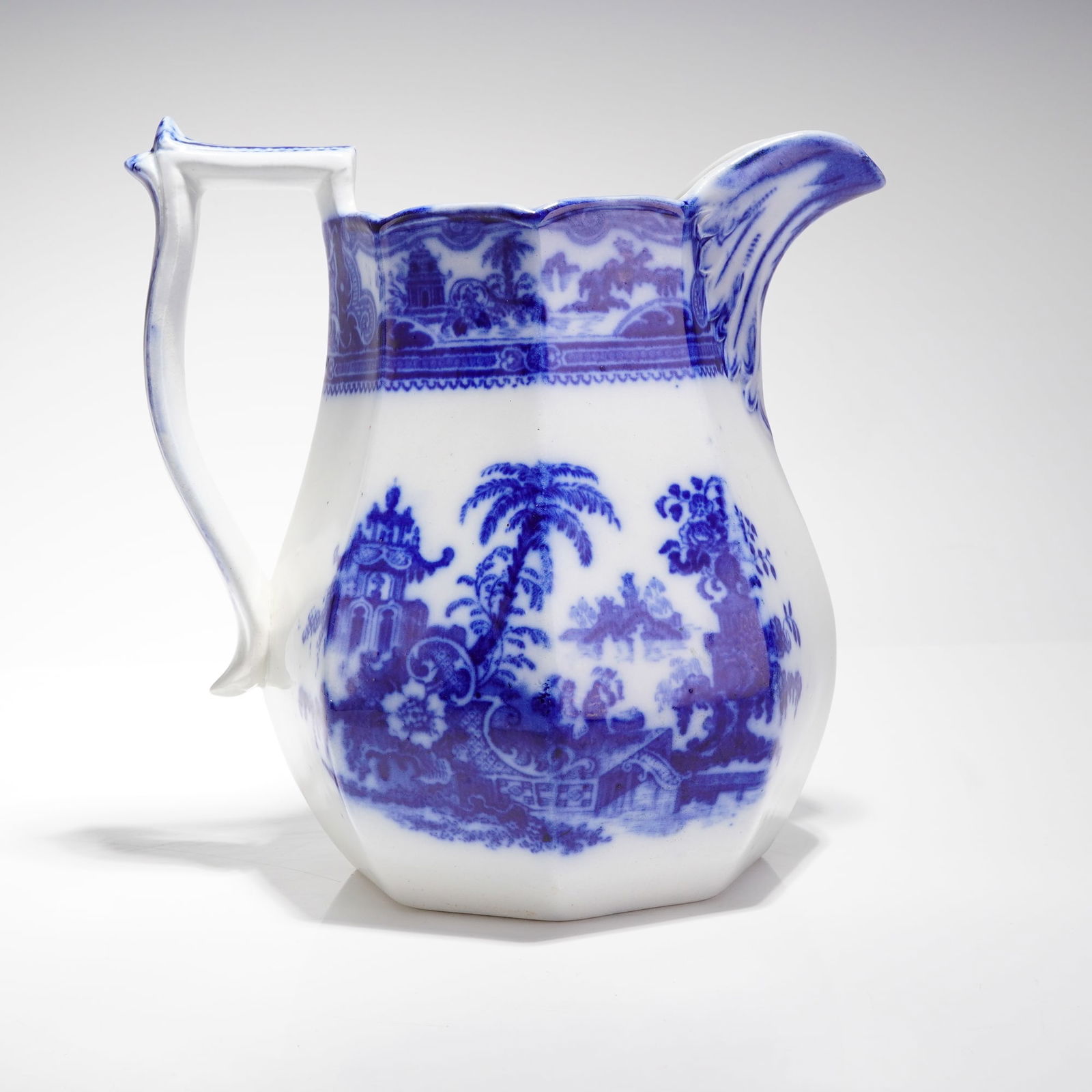 W. Adams Flow Blue Kyber Pattern Ceramic Pitcher: A single ceramic transferware pitcher manufactured by W. Adams in the Flow Blue technique, featuring the Kyber Pattern. The pitcher exhibits an octagonal body form with a scalloped rim and an angular