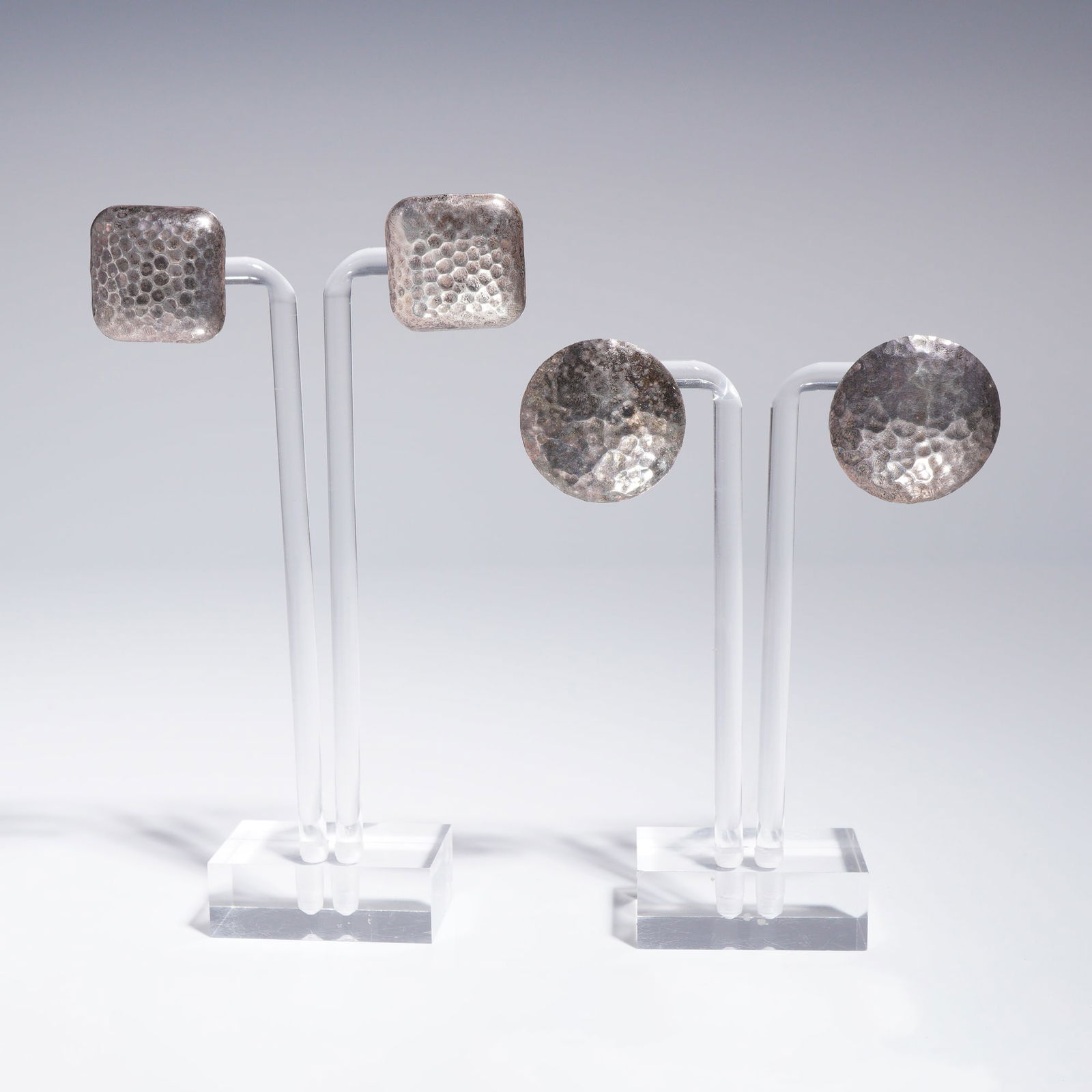 Two Pairs of Hammered Sterling Silver Stud Earrings: This lot comprises two distinct pairs of artisanal earrings. The earrings are crafted from sterling silver and feature a uniform, heavily hammered surface texture, giving them a rustic finish consiste