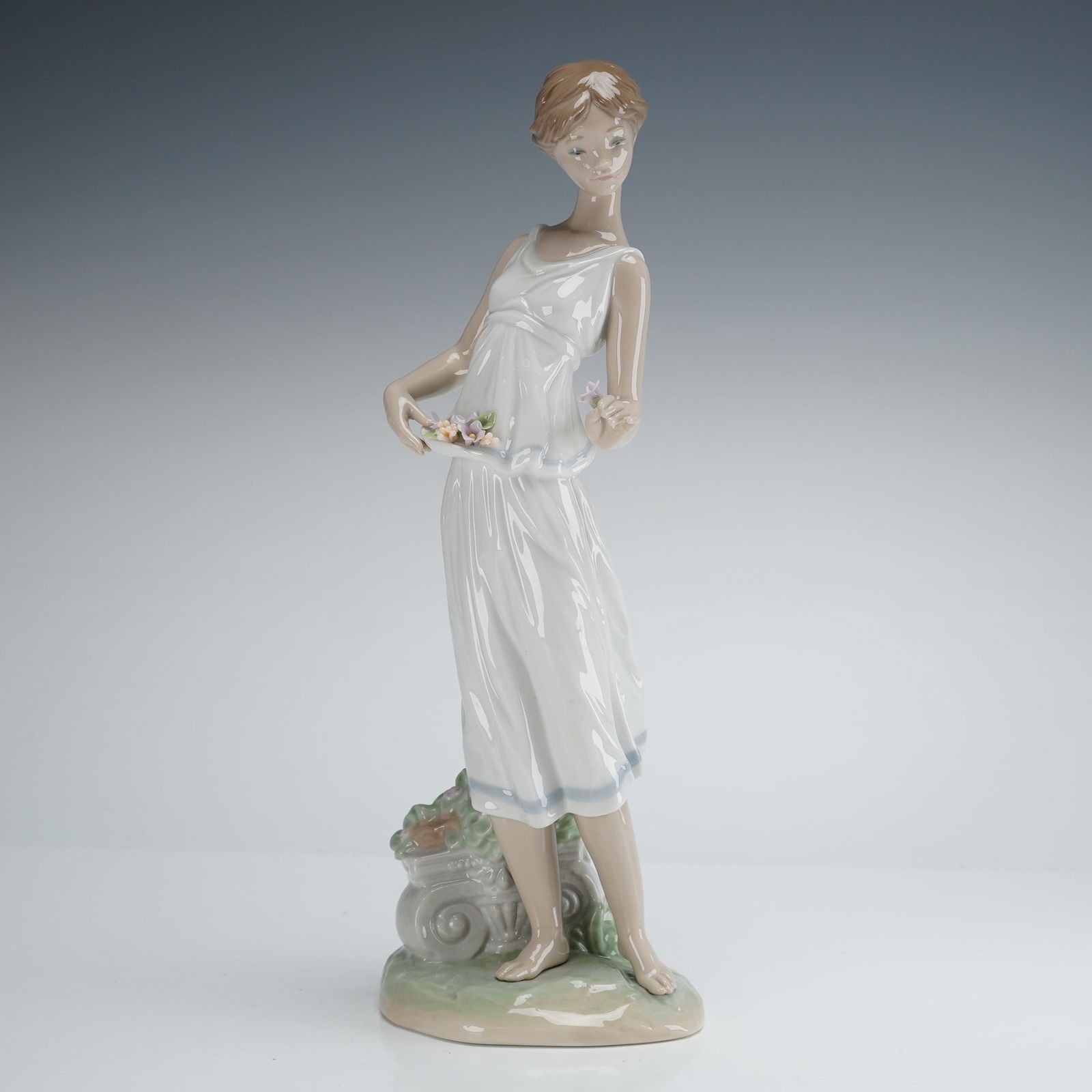 Lladro Flowers for a Goddess Figurine: A single Lladro porcelain figurine titled Flowers For A Goddess, number 1007709. This piece was designated as a Lladro Privilege item. The glazed porcelain figure depicts a young woman standing barefo