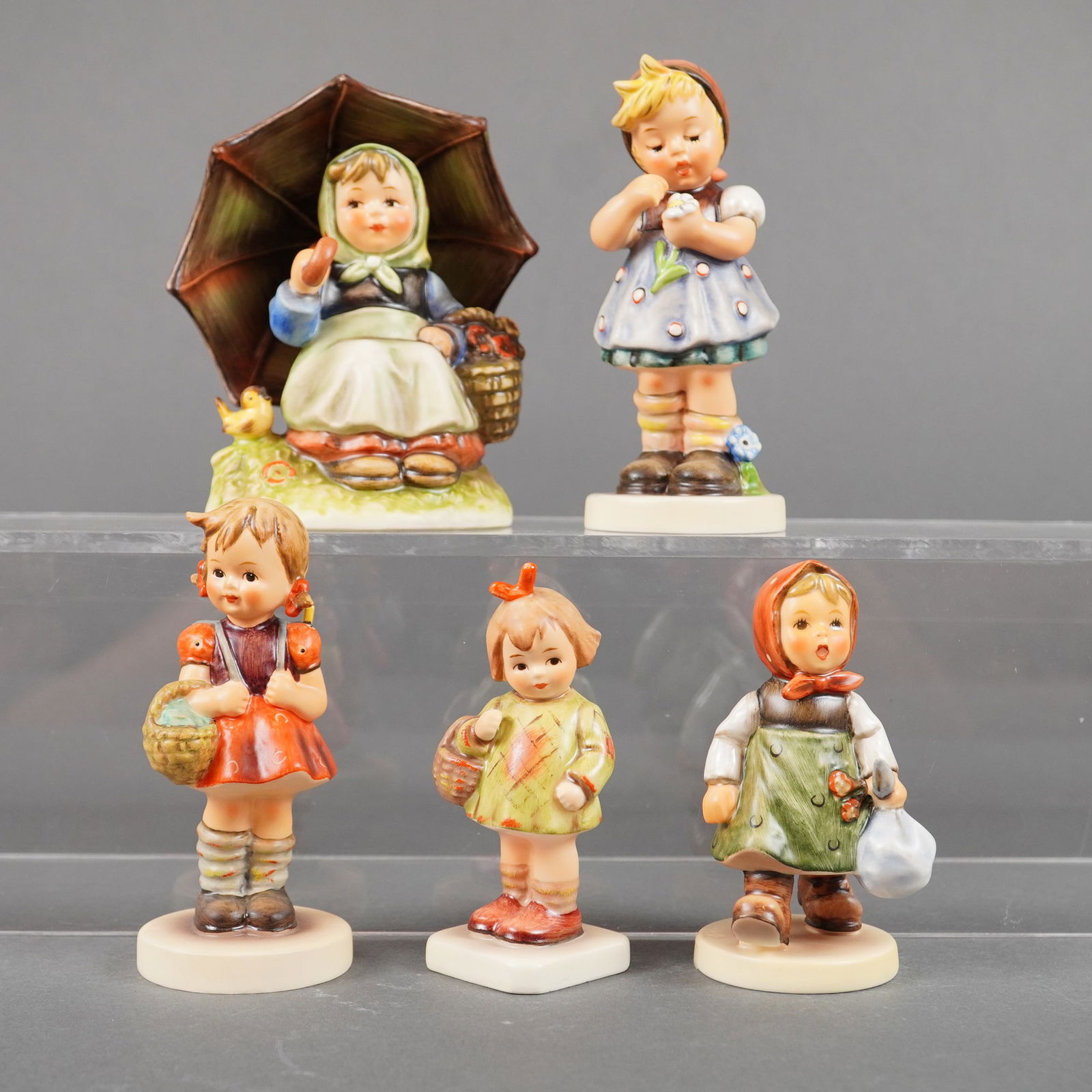 5 Goebel Hummel Figurines incl. Smiling Through #408: A collection of five hand-painted, glazed porcelain figurines manufactured by Goebel in West Germany, commonly known as Hummel figurines. The collection includes the iconic "Smiling Through" model #40