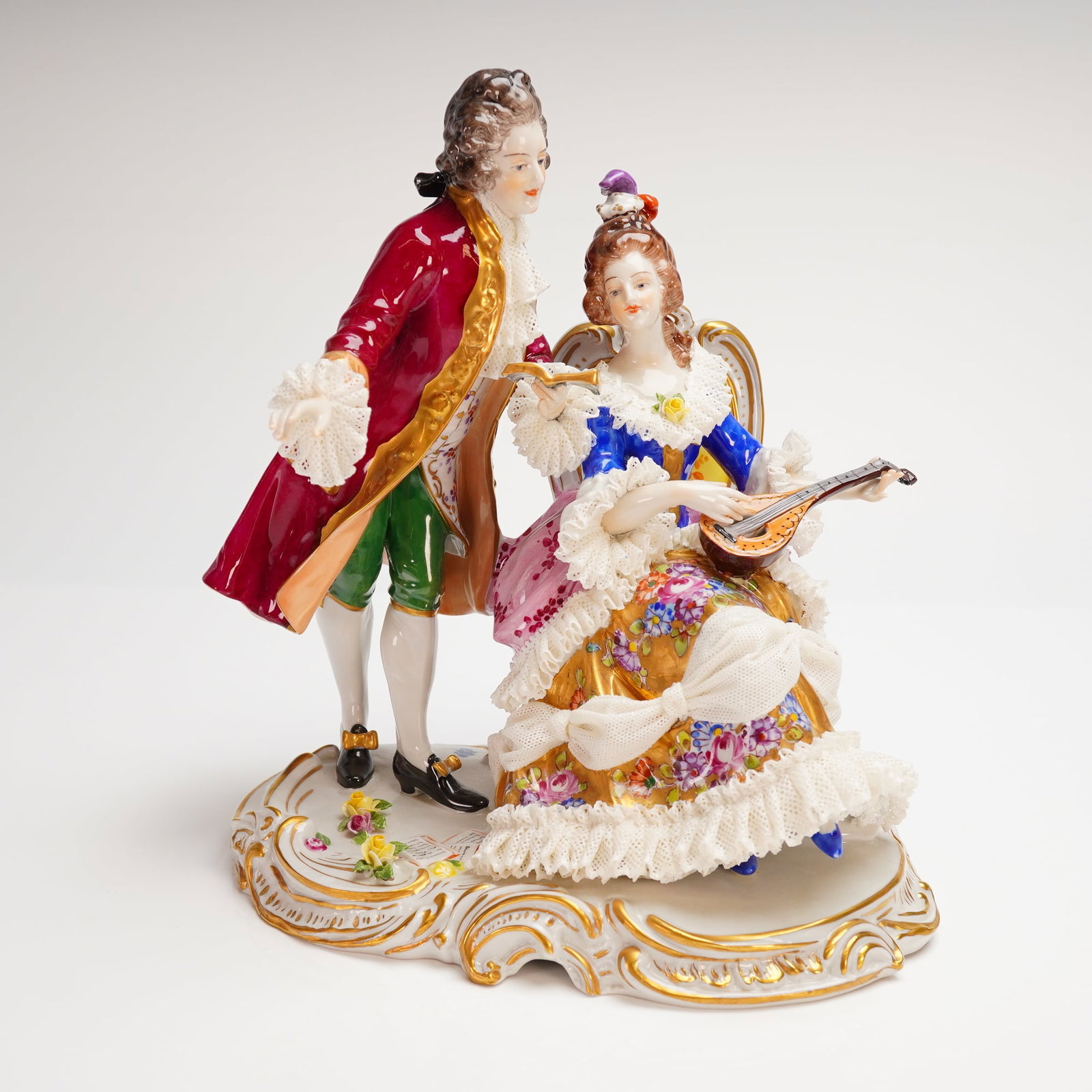 Volkstedt German Lace Porcelain Courting Musical Couple Figurine: Executed in the Rococo revival style, the group features a seated woman playing a mandolin or lute and a standing gentleman, both dressed in 18th-century aristocratic fashion. The porcelain is brightl