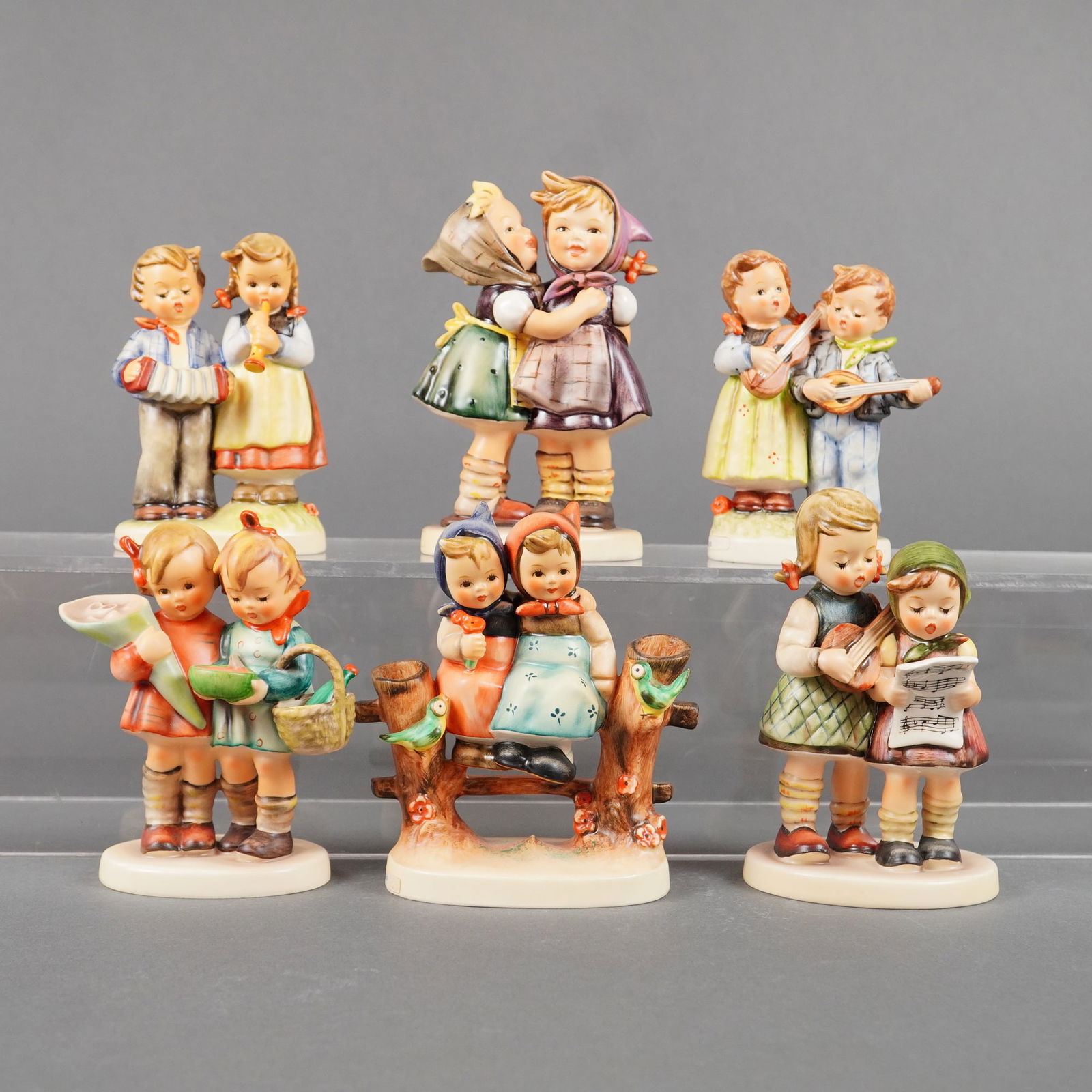 6 Goebel Hummel Figurines incl. Telling Her Secret: A collection of six hand-painted porcelain figurines executed in the style of Sister Maria Innocentia Hummel and manufactured by Goebel. The collection features pairs of children engaging in various a