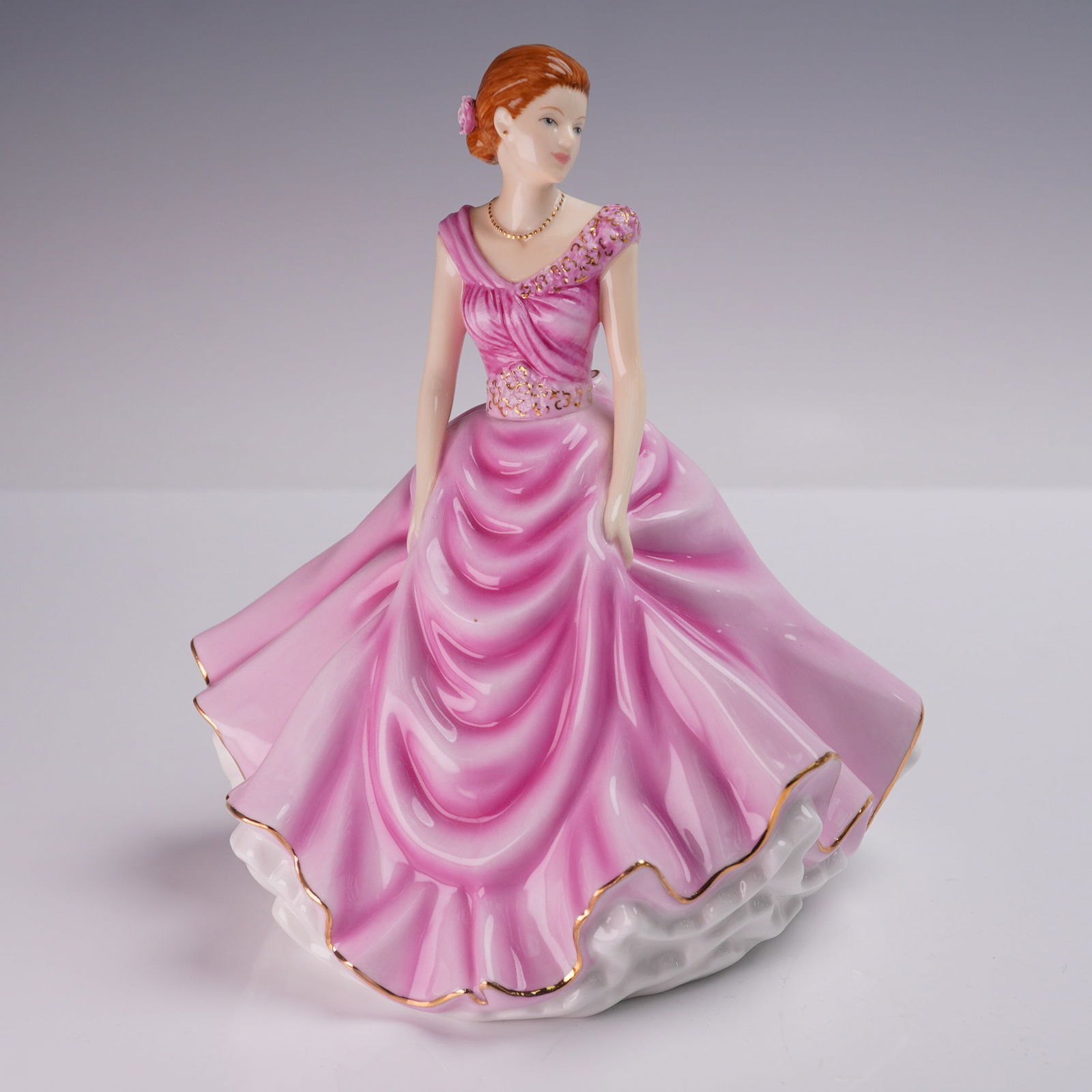 Royal Doulton Figurine, Donna HN5590 Signed: A bone china figurine depicting a young woman in a flowing pink gown with gilt trim and floral embellishments. Marked on the underside with Royal Doulton backstamp. Signed in gold ink by Michael Doult