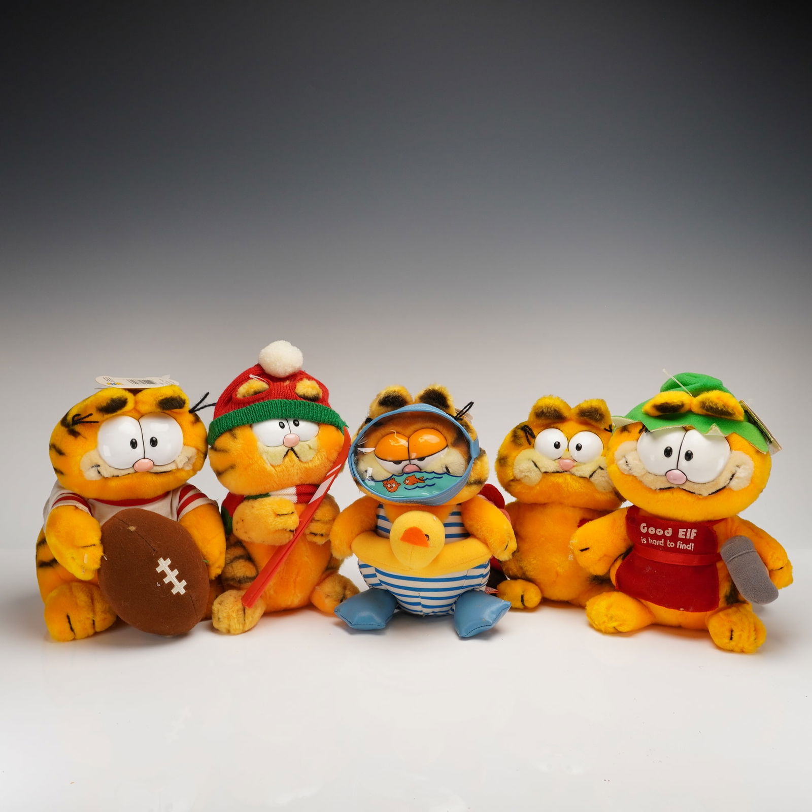A Collection of 5 Vintage Dakin Garfield Plush Toys: A collection of 5 vintage Garfield plush toys produced by R. Dakin & Company. The figures are constructed from synthetic orange and black striped fabric. Each figure depicts the iconic tabby cat in va