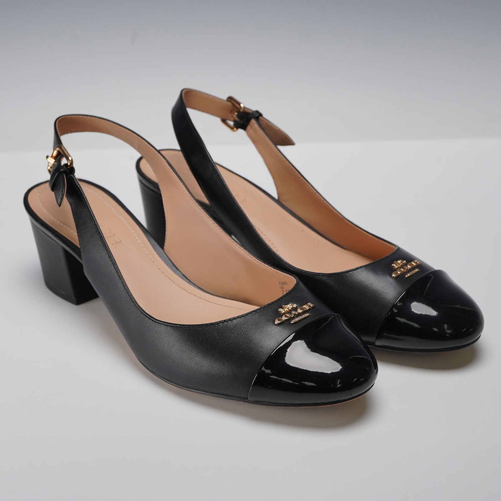 A Pair of Coach Erica Cap Toe Leather Slingback Pumps: A pair of contemporary womens Coach Erica Cap Toe Leather Slingback Pumps. Crafted from black matte leather with contrasting black patent leather toe caps, each shoe features a gold-tone metal COACH b