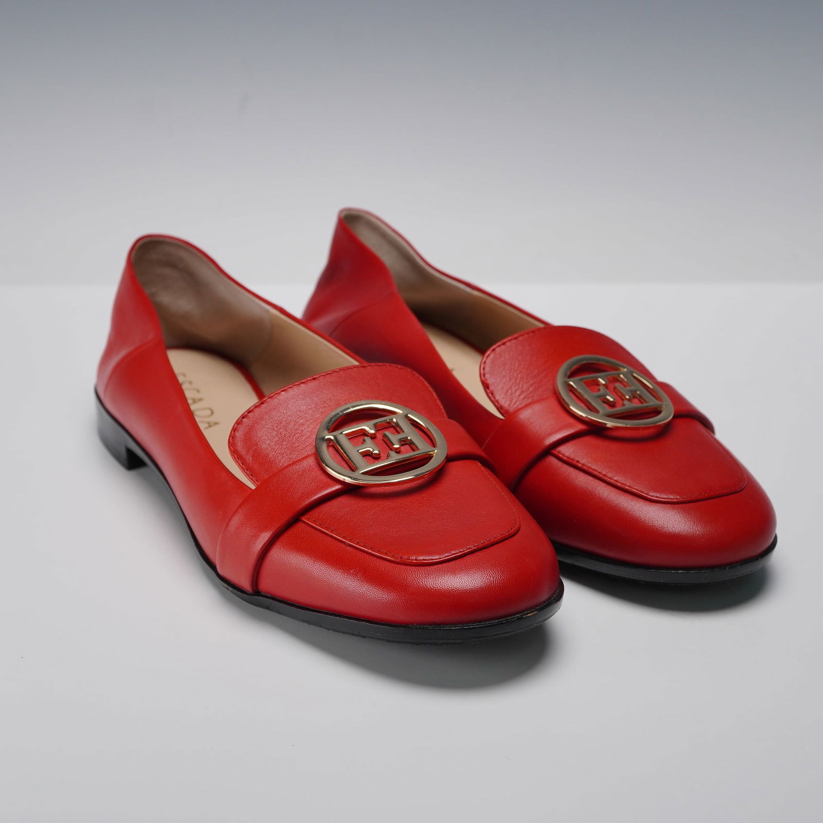 A Pair of ESCADA Red Leather Loafers: A pair of ESCADA red leather loafers. These contemporary slip-on loafers are crafted from vibrant red leather, featuring a rounded toe and a low black block heel. Each shoe is adorned with a prominent