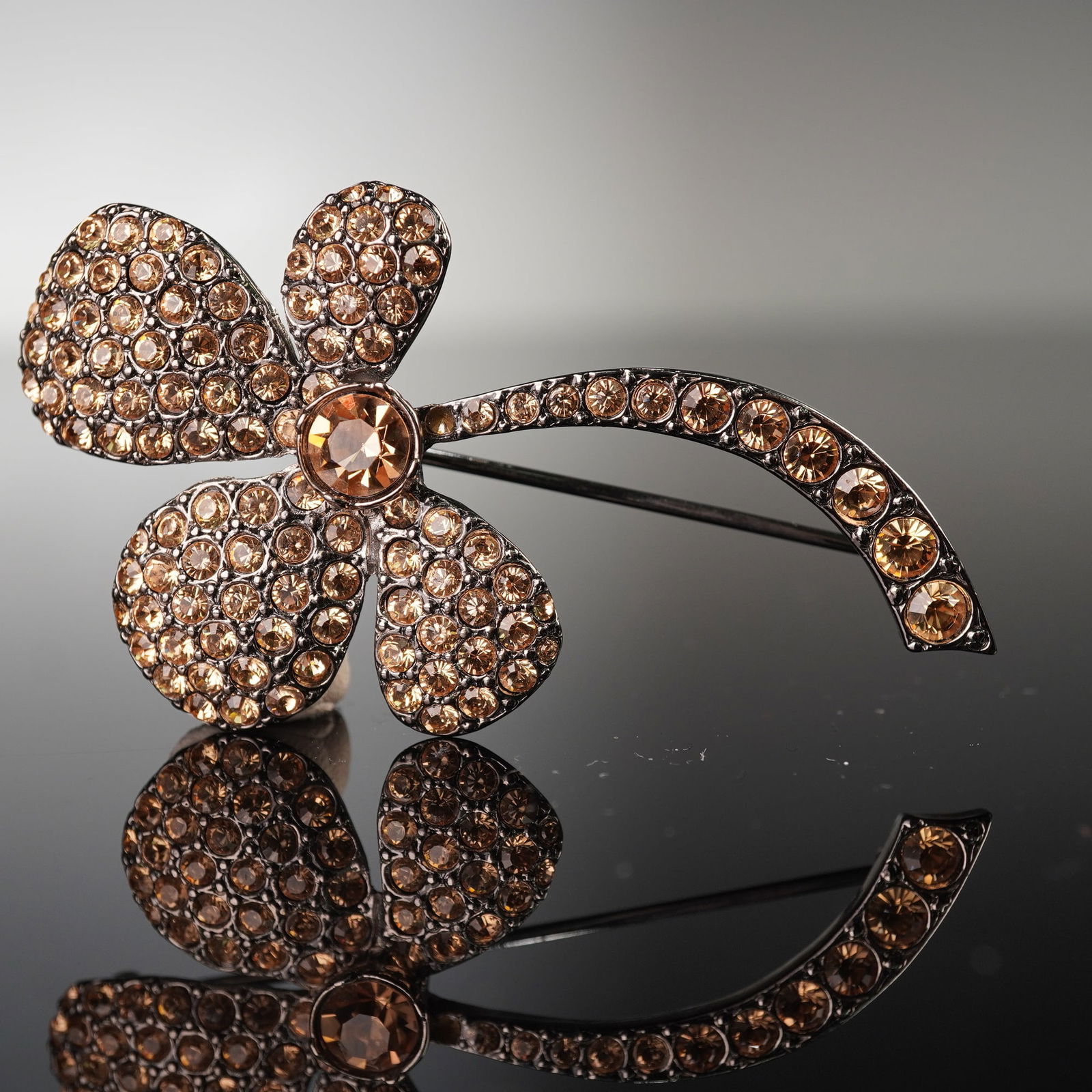 Sonia Rykiel Paris Pave-Set Amber Swarovski Rhinestone Clover Brooch: A Sonia Rykiel pave-set Swarovski rhinestone brooch, designed as a four-leaf clover with an arced stem. It is constructed from a dark-toned metal, possibly gunmetal or an antiqued silver-tone finish,