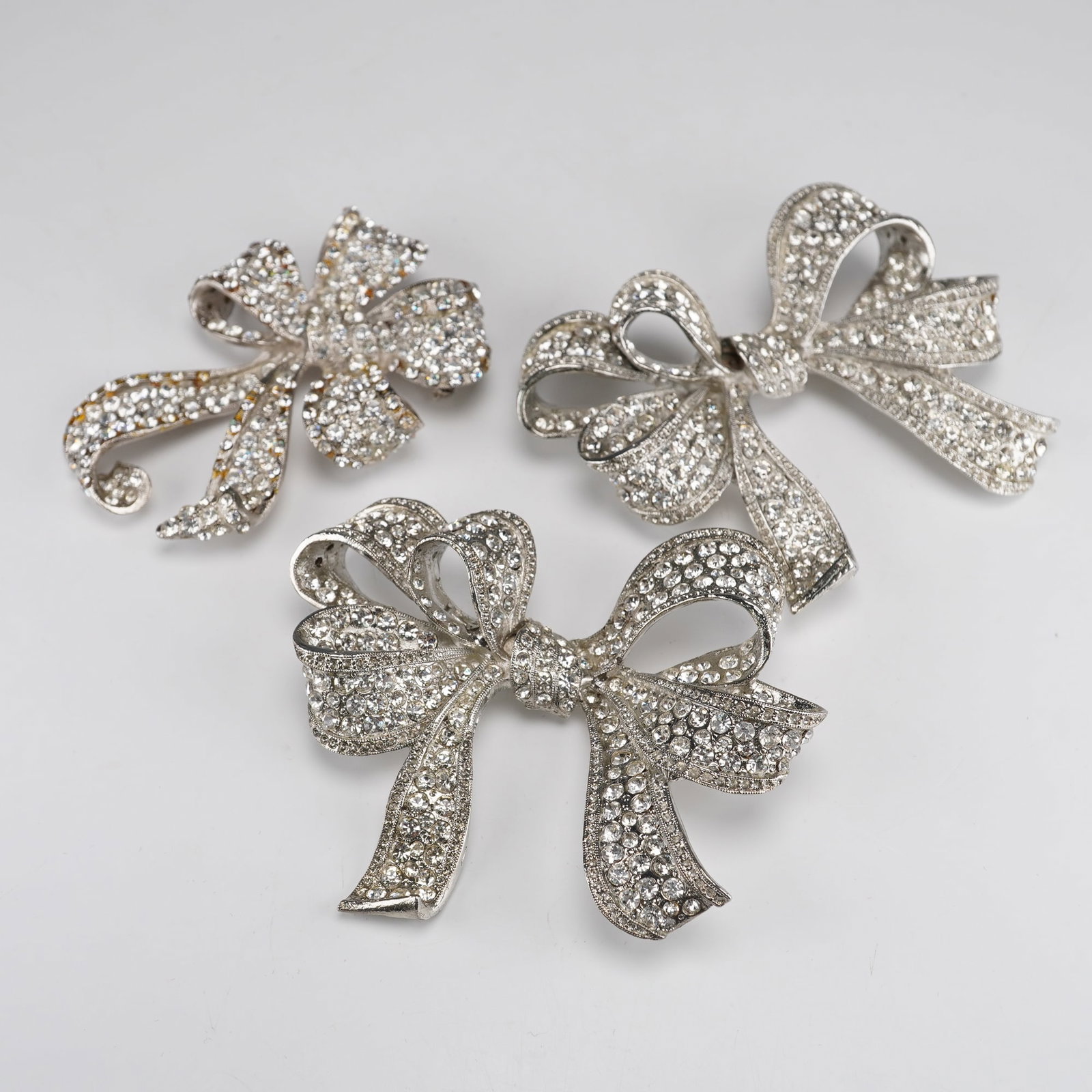 3pc Barrera Silver-Tone Rhinestone Bow Brooches: A group of three brooches, all marked 'BARRERA' on their reverse. Each brooch is crafted from silver-tone metal and intricately adorned with numerous clear, faceted rhinestones in a pave setting. The 