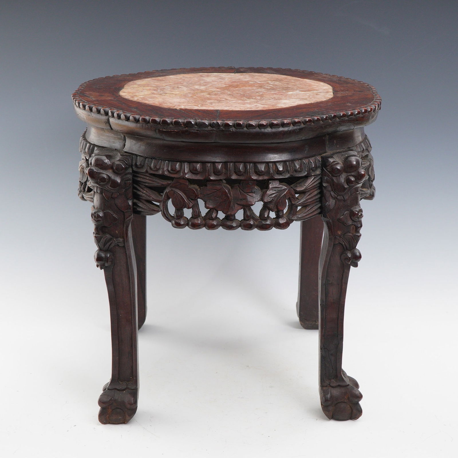 Chinese Carved Hardwood Marble Top Stand: Early 20th century Chinese carved hardwood stand featuring an inset circular pink variegated marble top. The apron is adorned with intricately carved grapevines and foliage, with detailed guardian lio