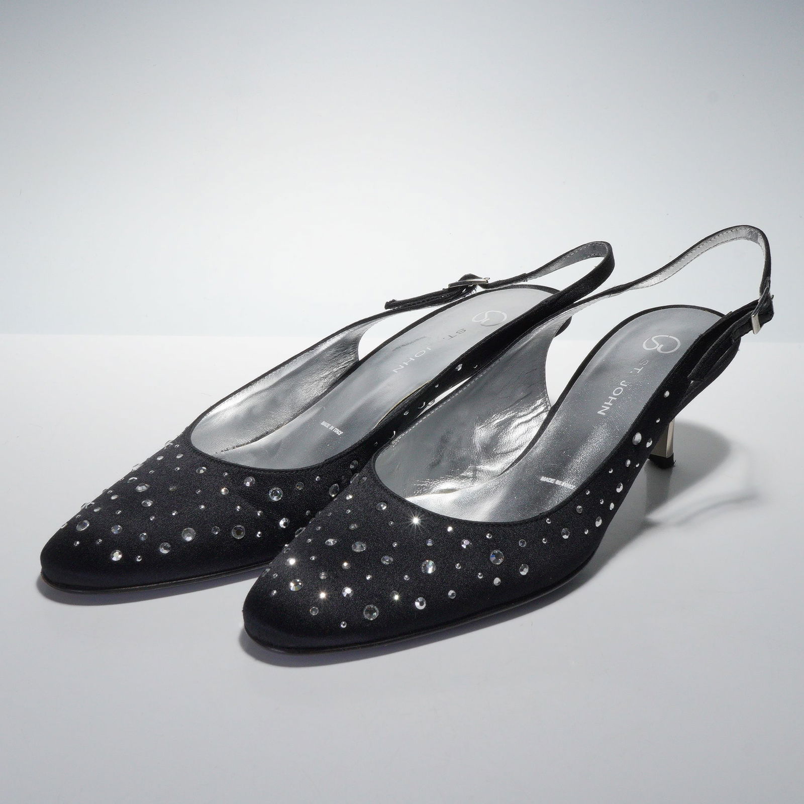 A Pair of St. John Black Fabric Rhinestone Embellished Slingback Heels: A pair of St. John black fabric slingback heels, featuring pointed toes and medium-height, flared silver-toned metallic heels. The vamp of each shoe is extensively adorned with clear, faceted rhinesto