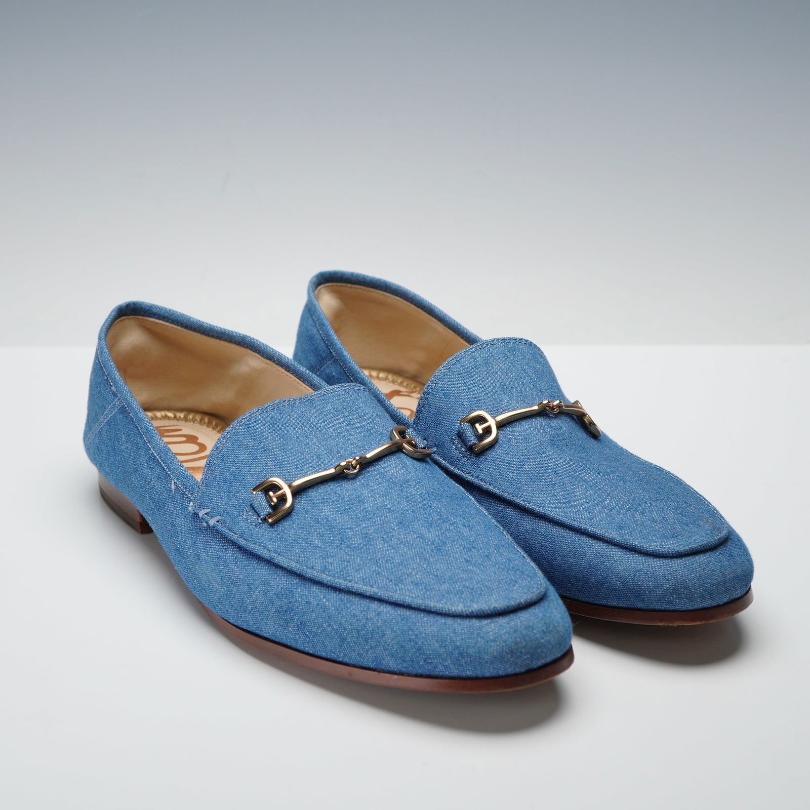 A Pair of Sam Edelman Loraine Bit Blue Denim Loafers: A pair of womens Sam Edelman Loraine bit loafers with a blue denim upper and gold tone snaffle hardware across the vamp. The shoes have light brown leather insoles stamped Sam Edelman in gold script a